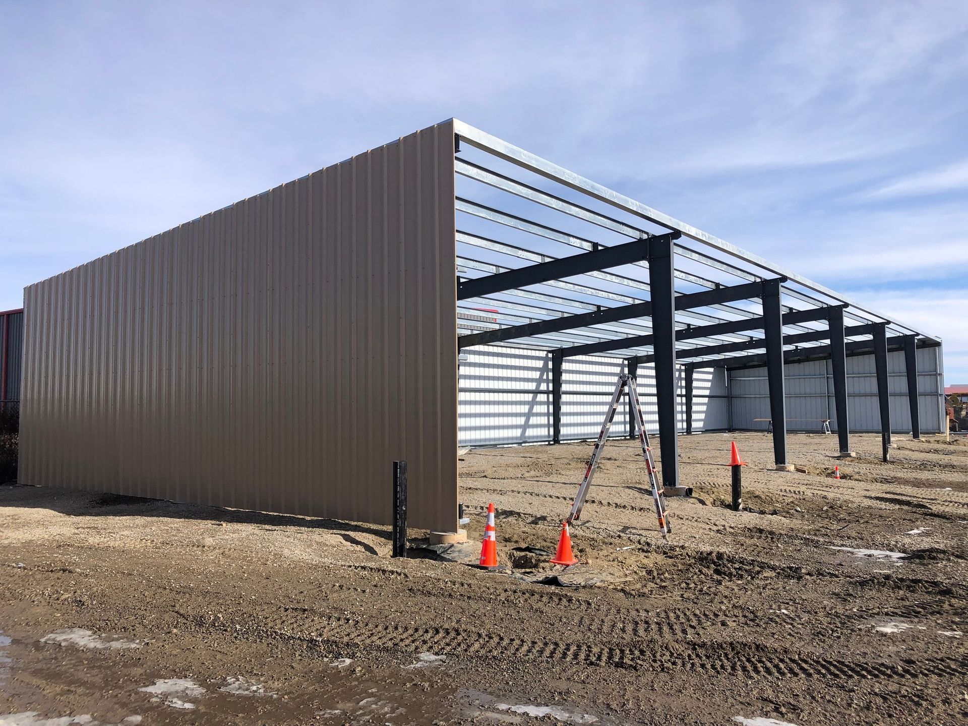 A large metal building is being built in a dirt field.