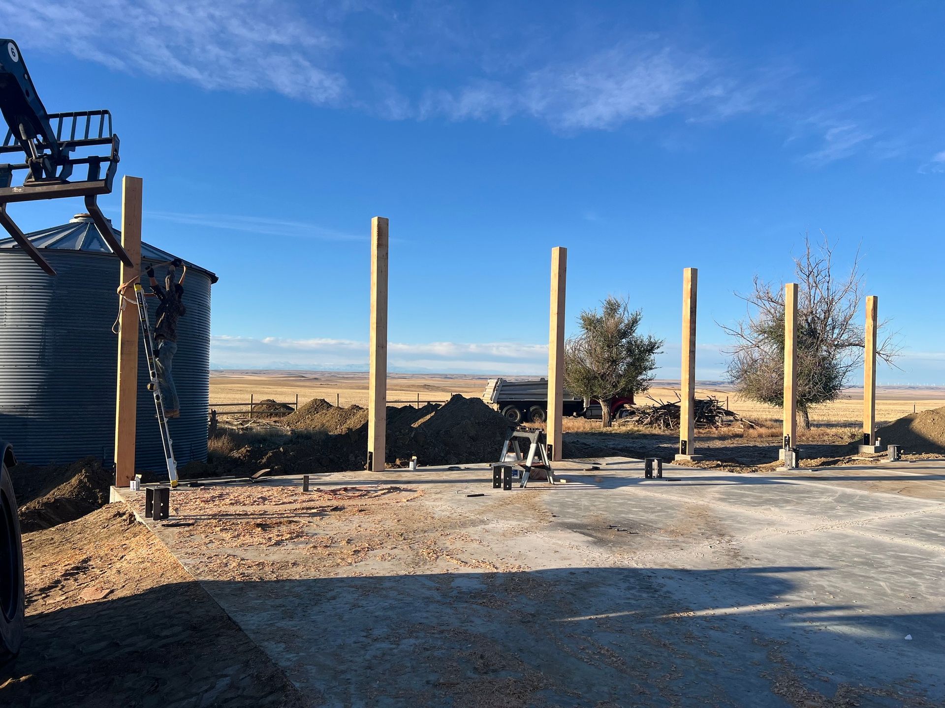 A row of wooden posts are being built in a dirt field.