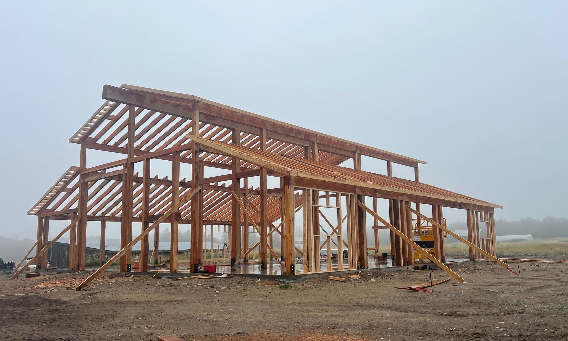 A large wooden structure is being built in a field on a foggy day.