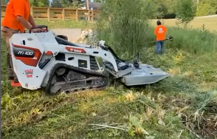 A man is using a tractor to cut grass in a field.