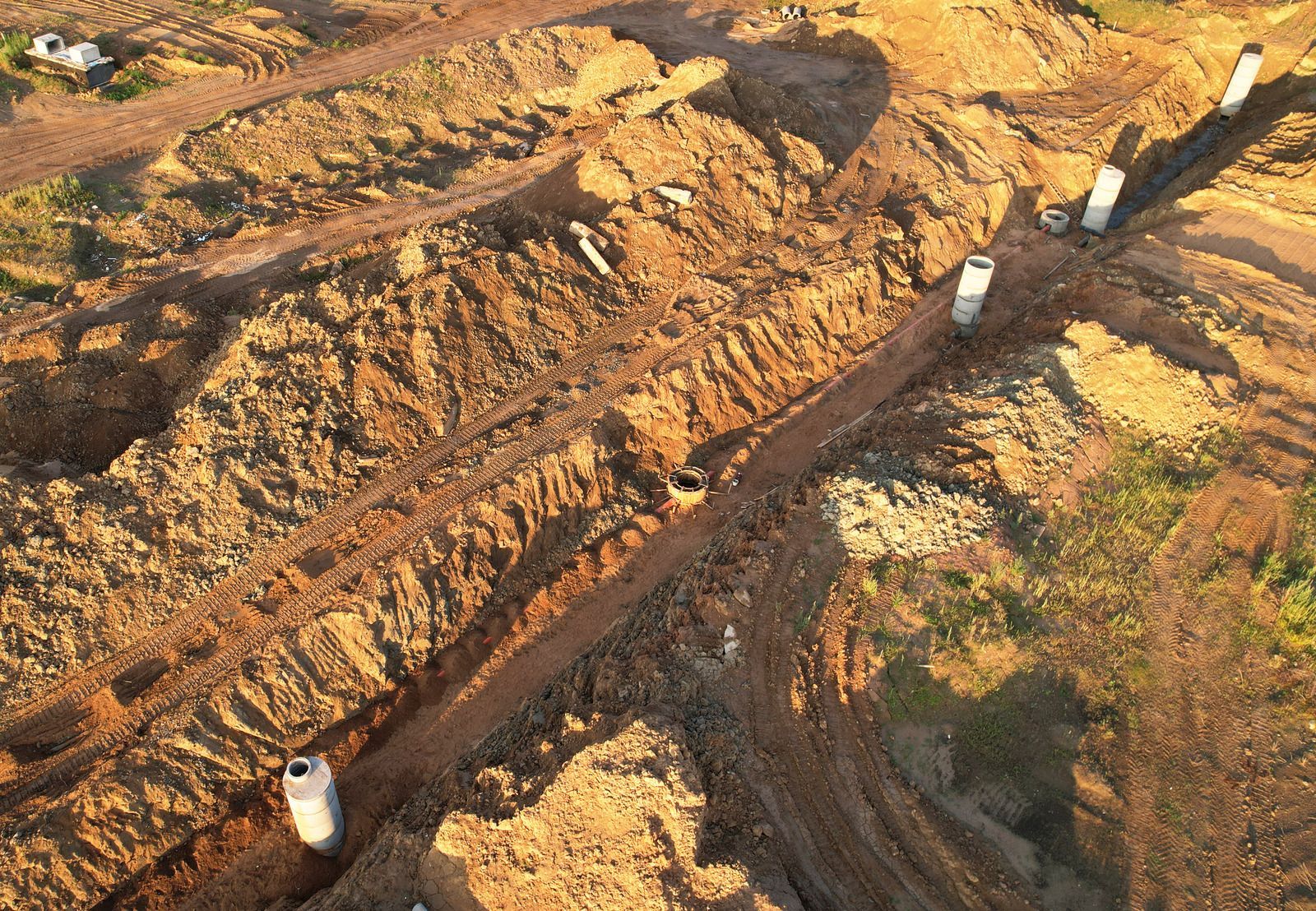 Aerial view of construction site with trenches and concrete pipes in brown dirt.