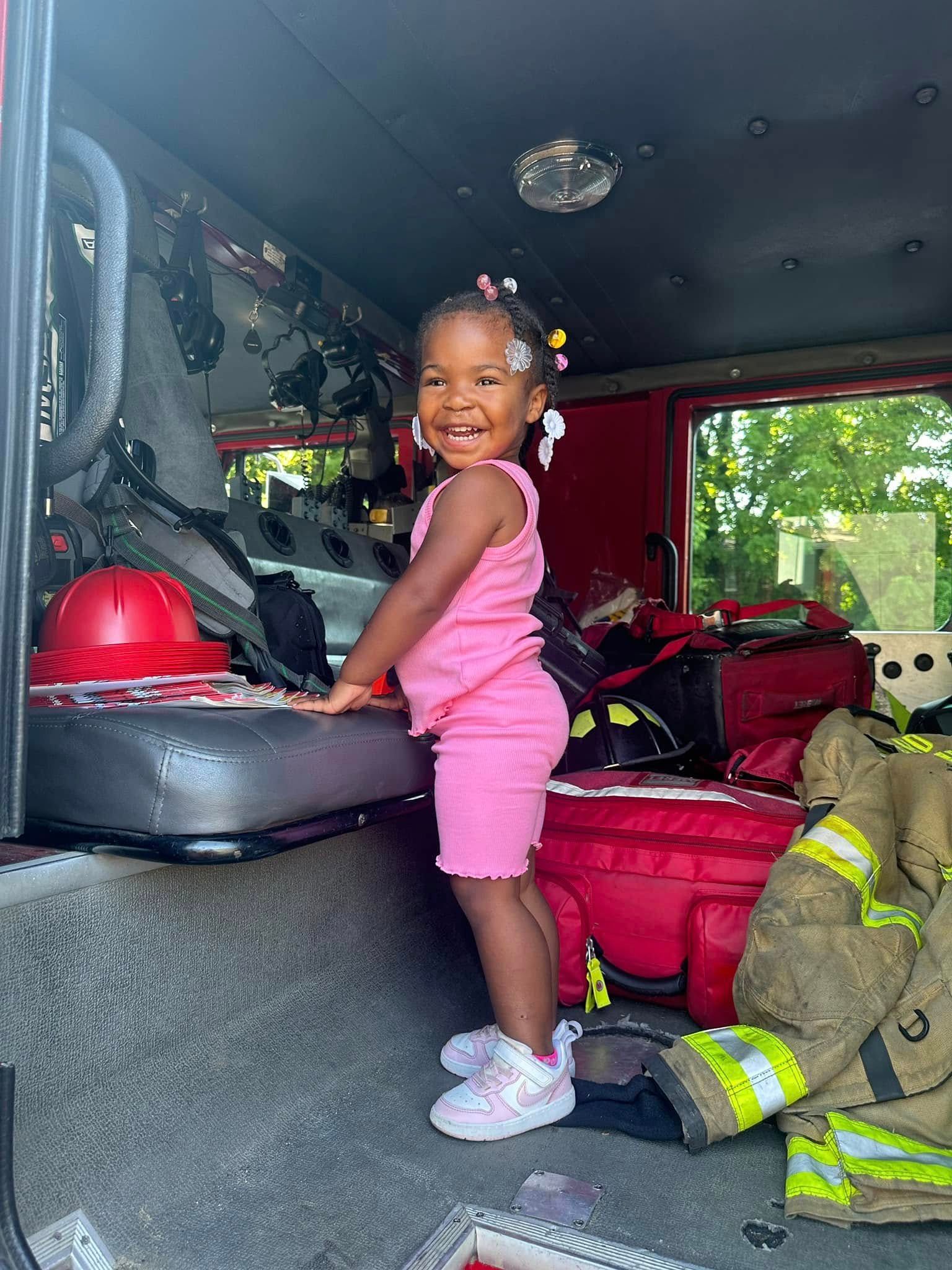A little girl is standing in the back of a fire truck.