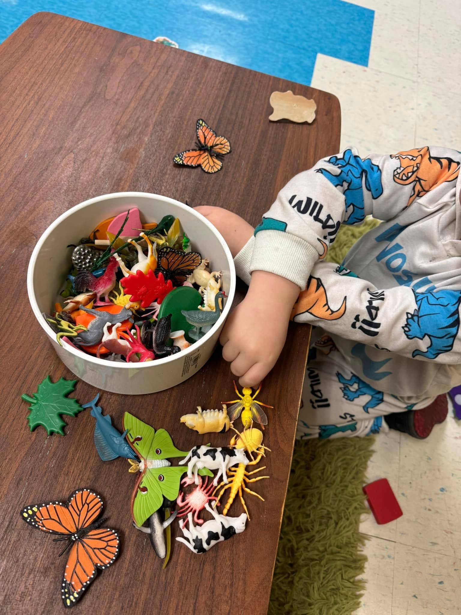 A child is playing with a bowl of toy animals on a table.