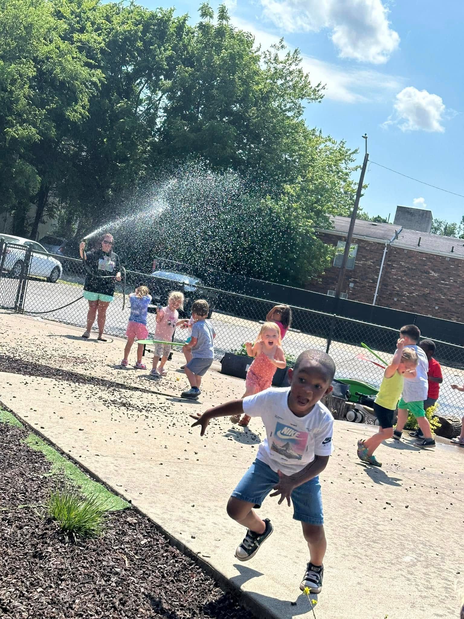 A group of children are playing in a park with a hose spraying water.