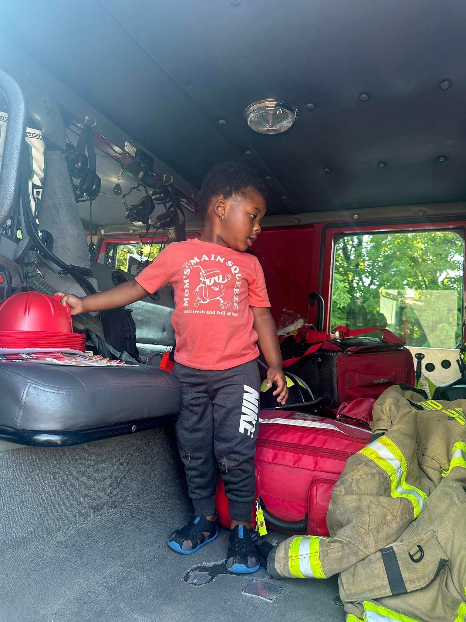 A little boy is standing in the back of a fire truck.