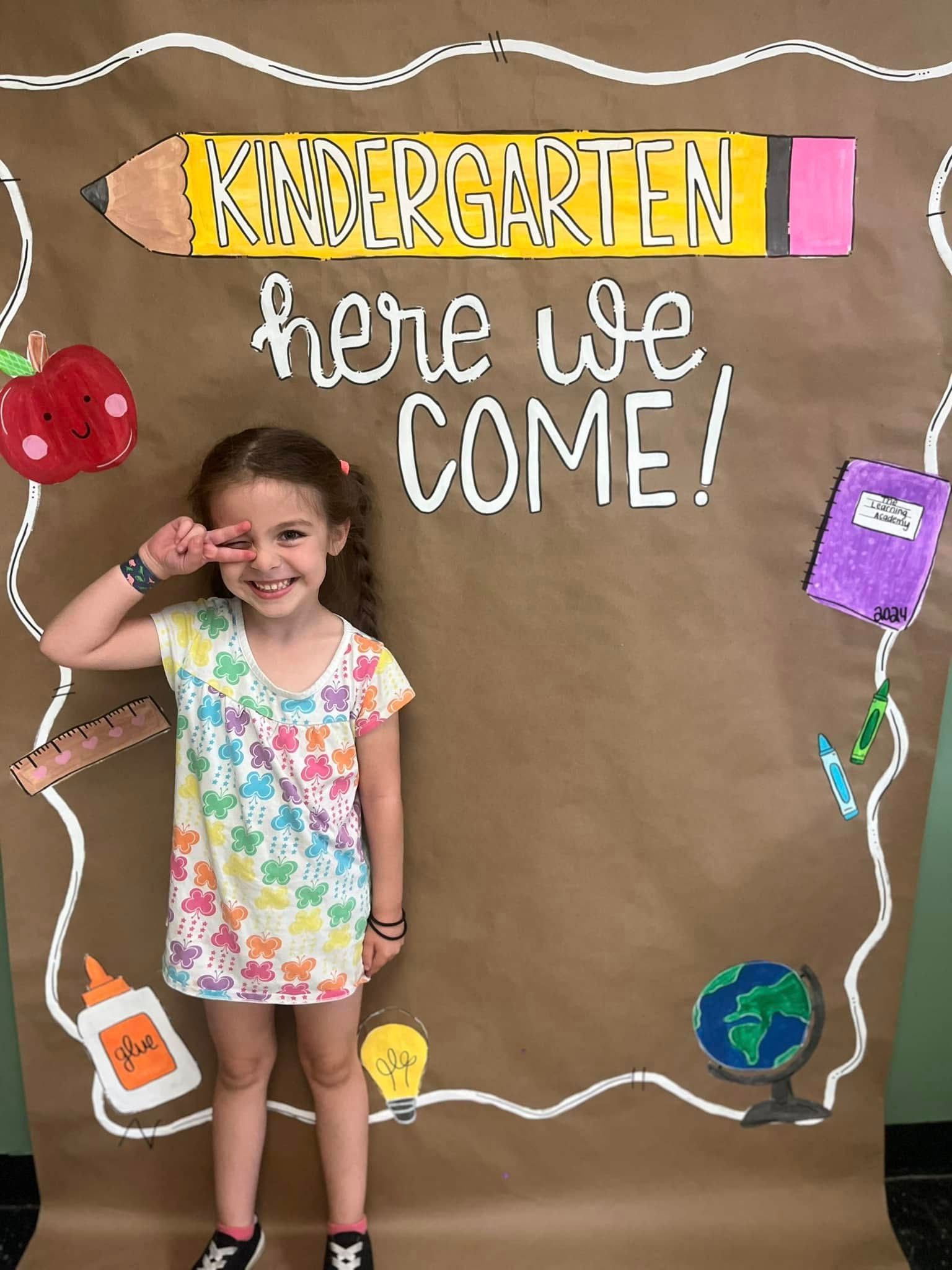 A little girl is standing in front of a sign that says `` here we come ''.