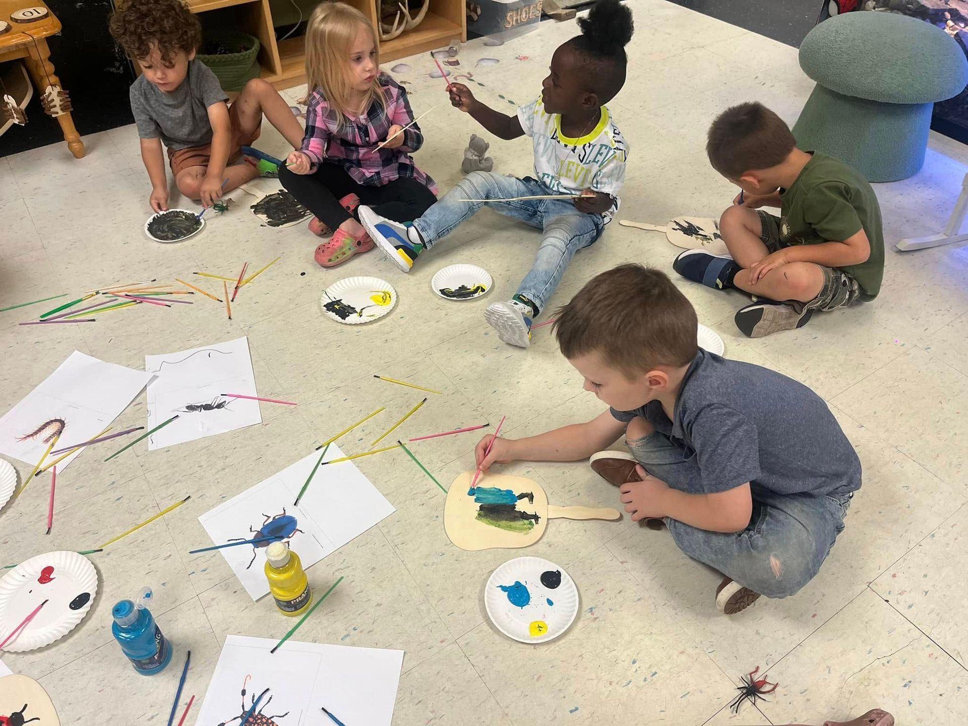 A group of children are sitting on the floor painting.