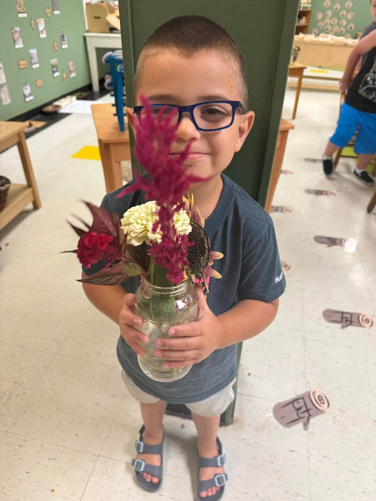 A young boy wearing glasses is holding a vase of flowers.