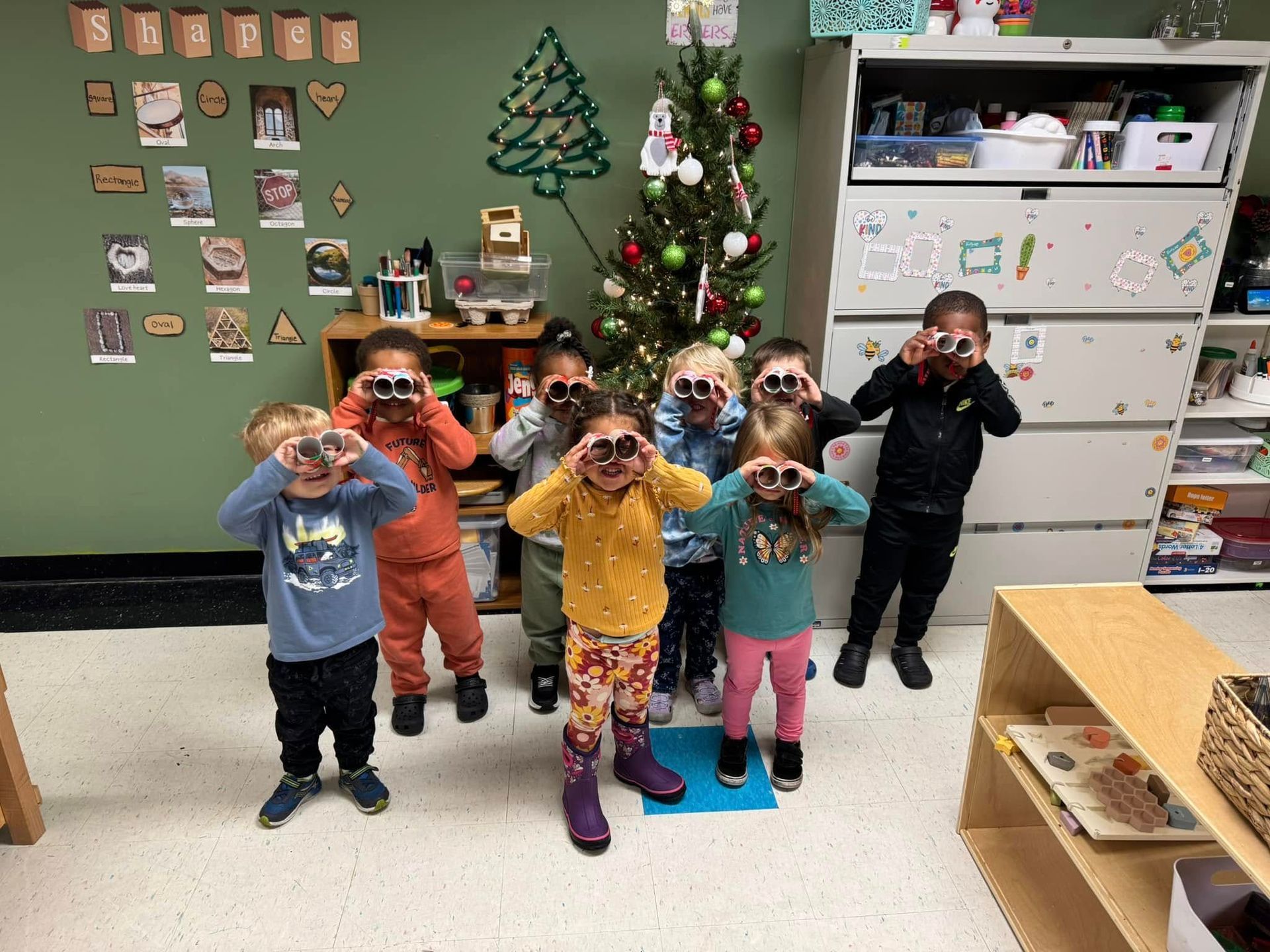 A group of children are standing in front of a christmas tree looking through binoculars.
