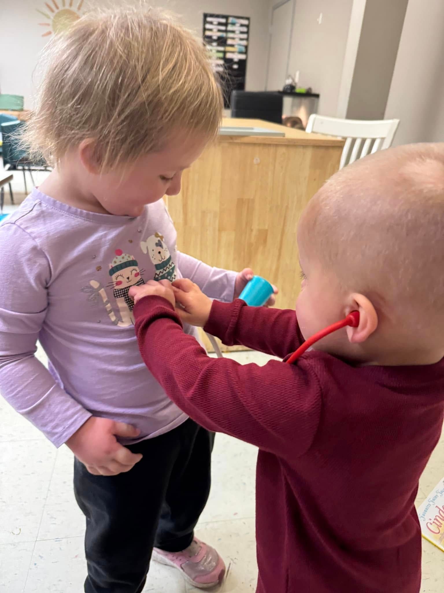 A little boy is playing with a stethoscope on a little girl 's chest.