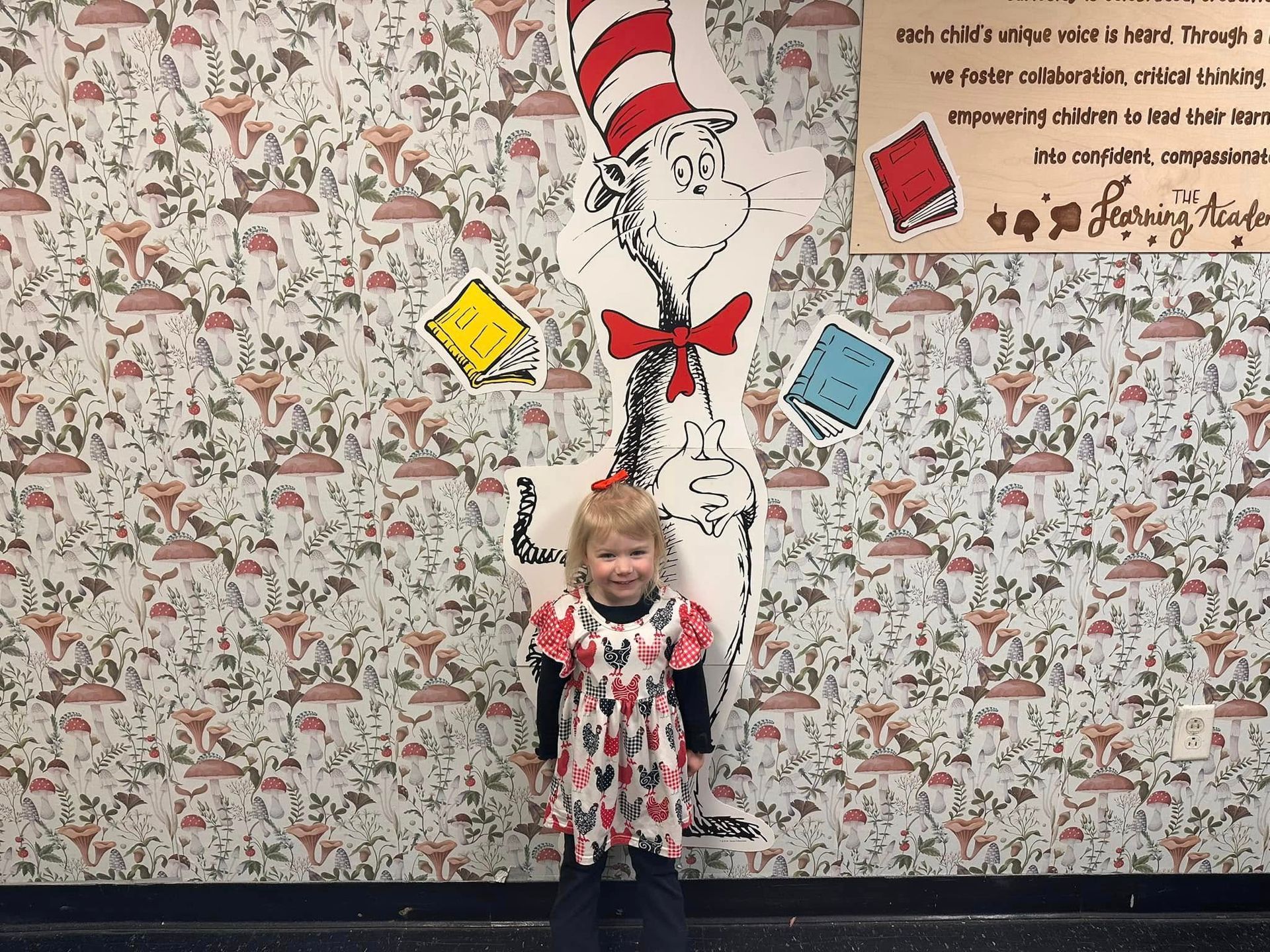 A little girl is standing in front of a cat in the hat mural.
