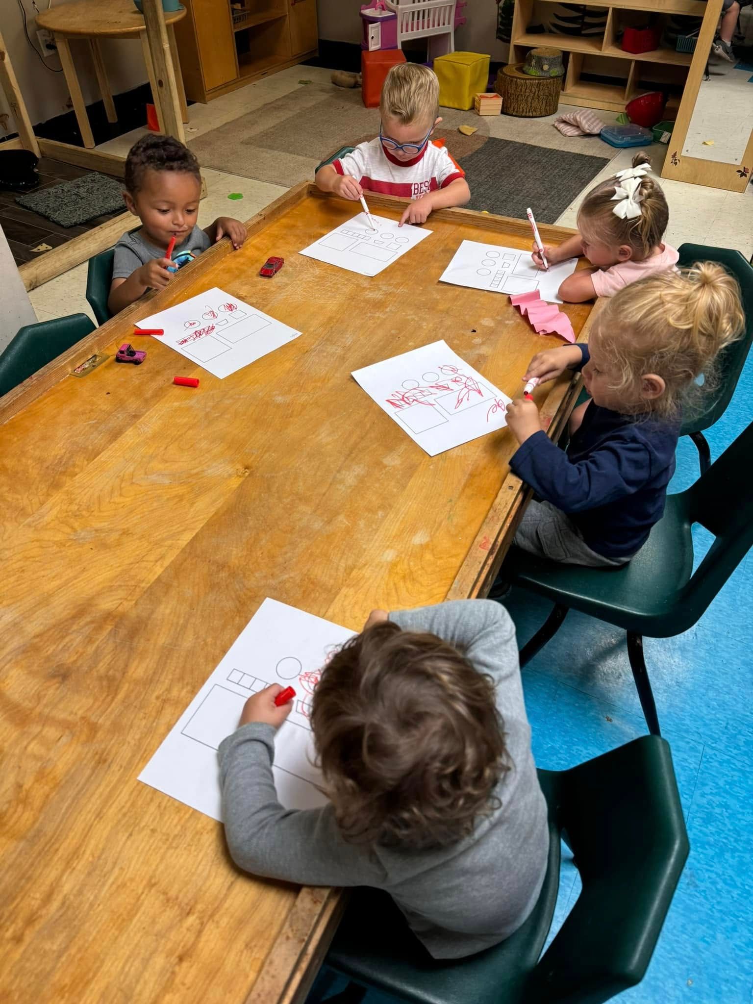 A group of children are sitting at a table drawing with crayons.