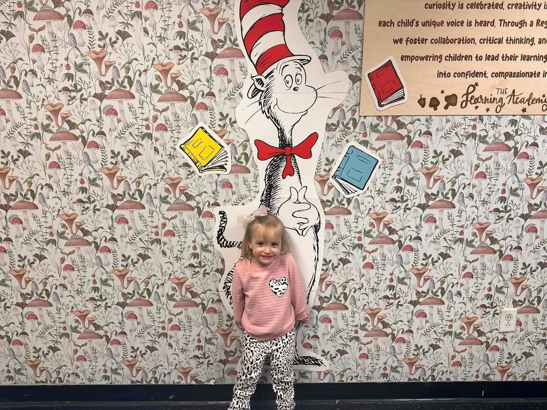 A little girl is standing in front of a cat in the hat mural.