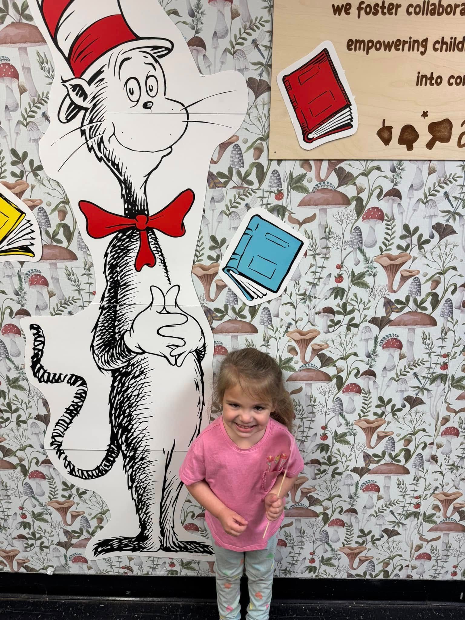 A little girl is standing in front of a cat in the hat mural.