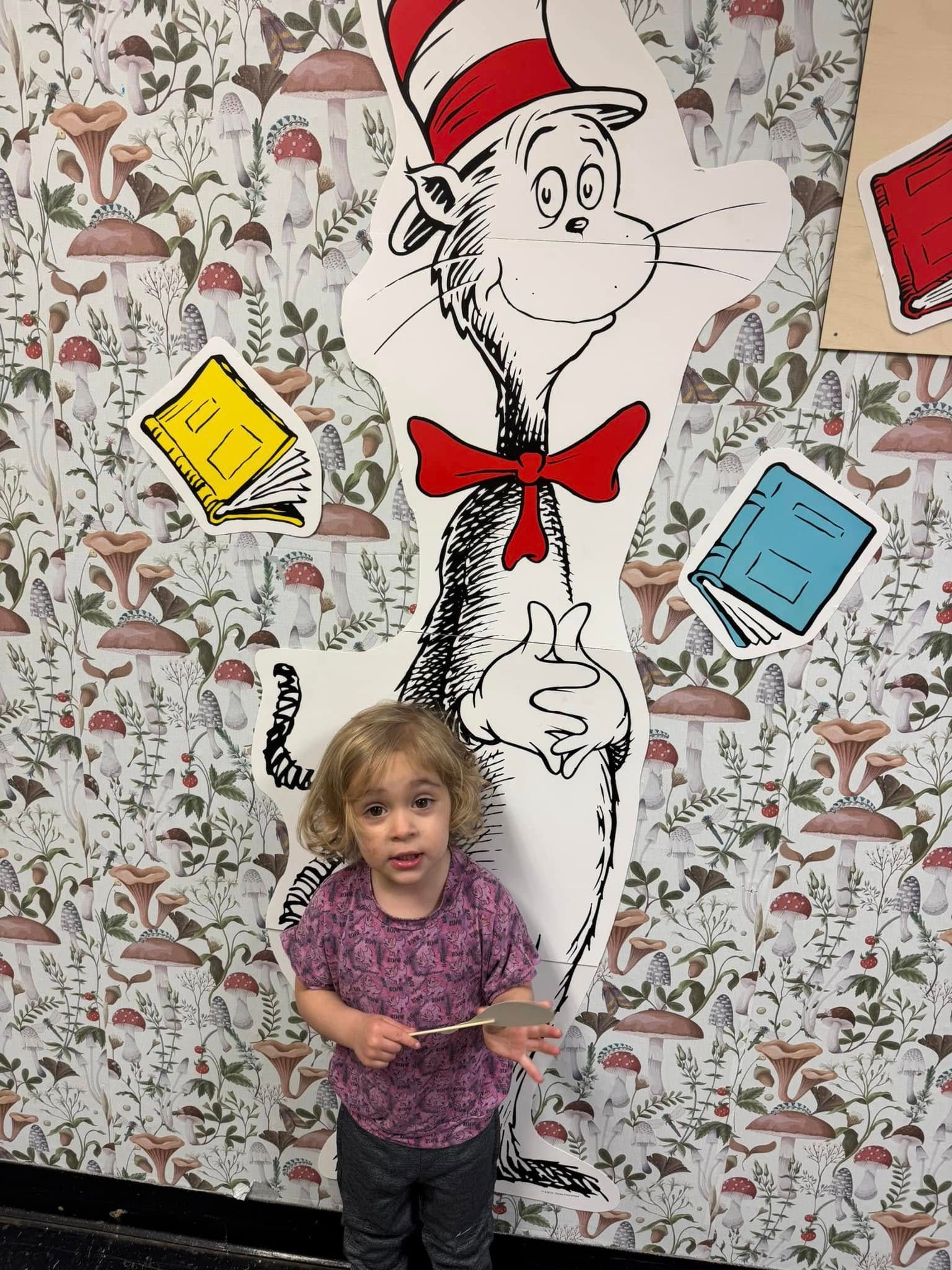 A little girl is standing in front of a cat in the hat statue.
