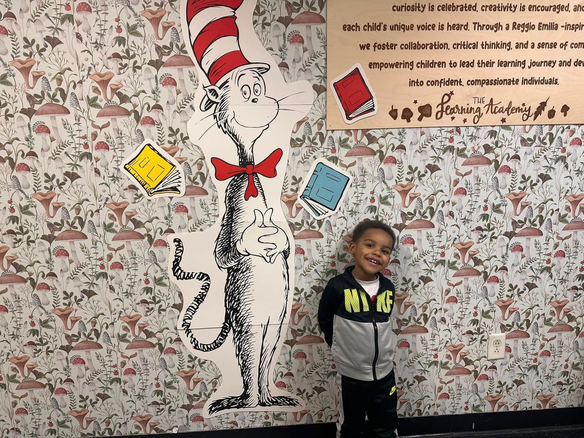 A young boy is standing in front of a cat in the hat mural.