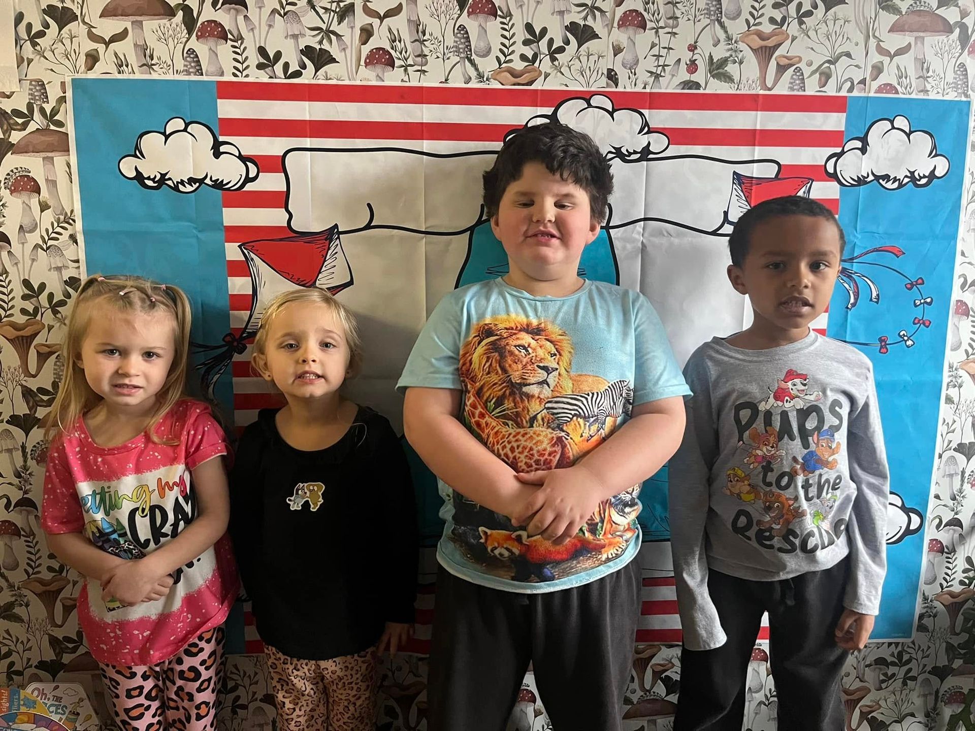 A group of children are standing in front of a cat in the hat wall.