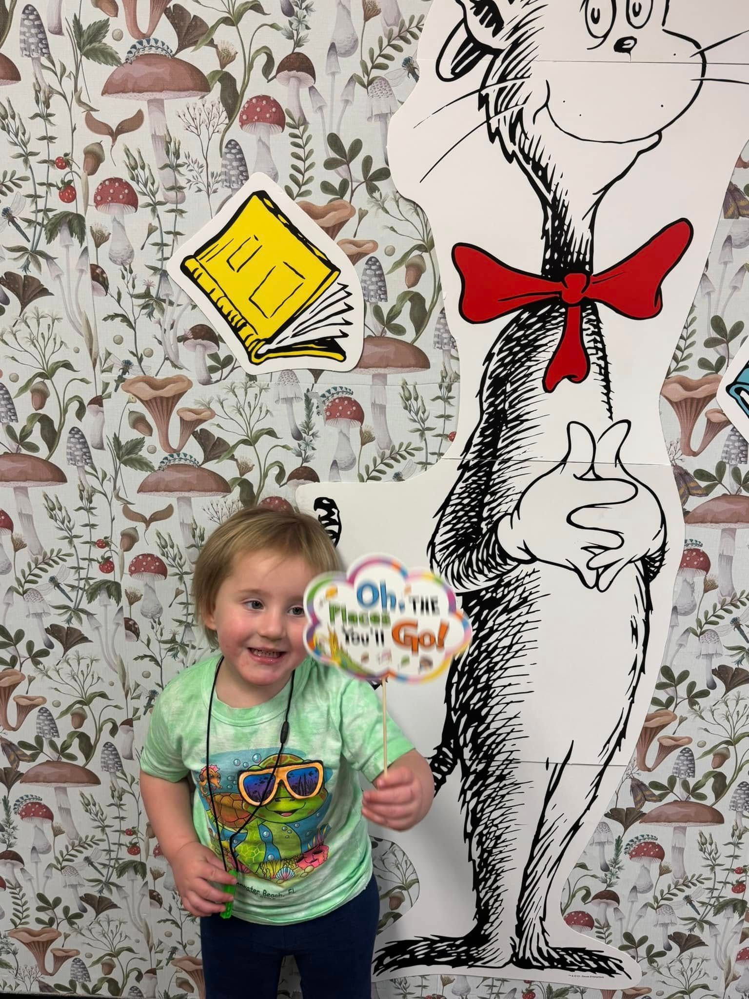 A little boy is standing in front of a cardboard cutout of dr. seuss.