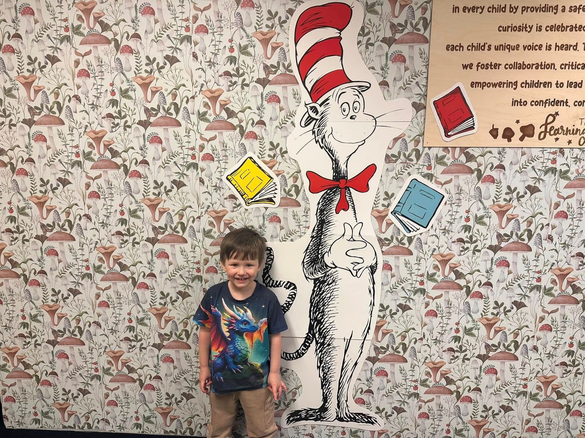 A little boy is standing in front of a cat in the hat statue.