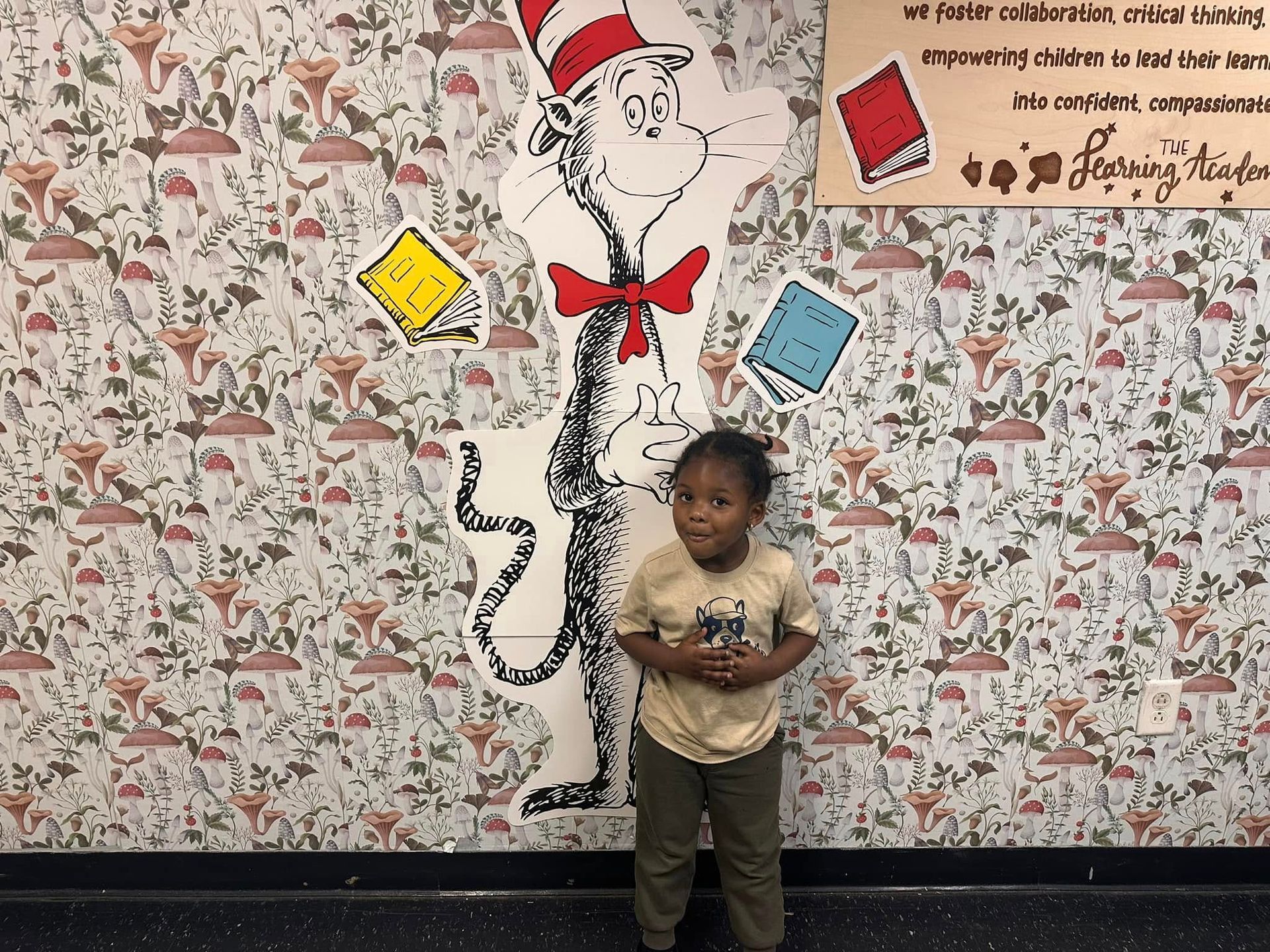A little girl is standing in front of a cat in the hat mural.