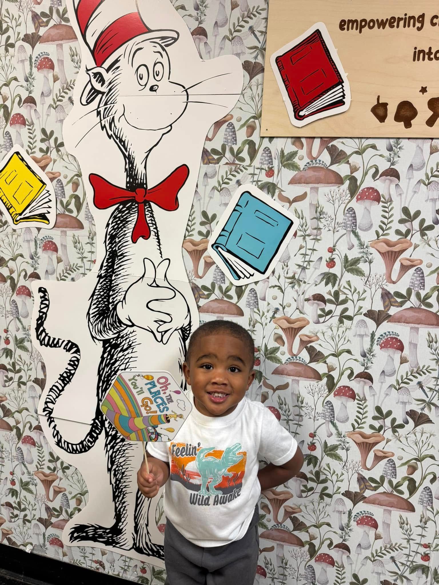 A little boy is standing in front of a cat in the hat mural.