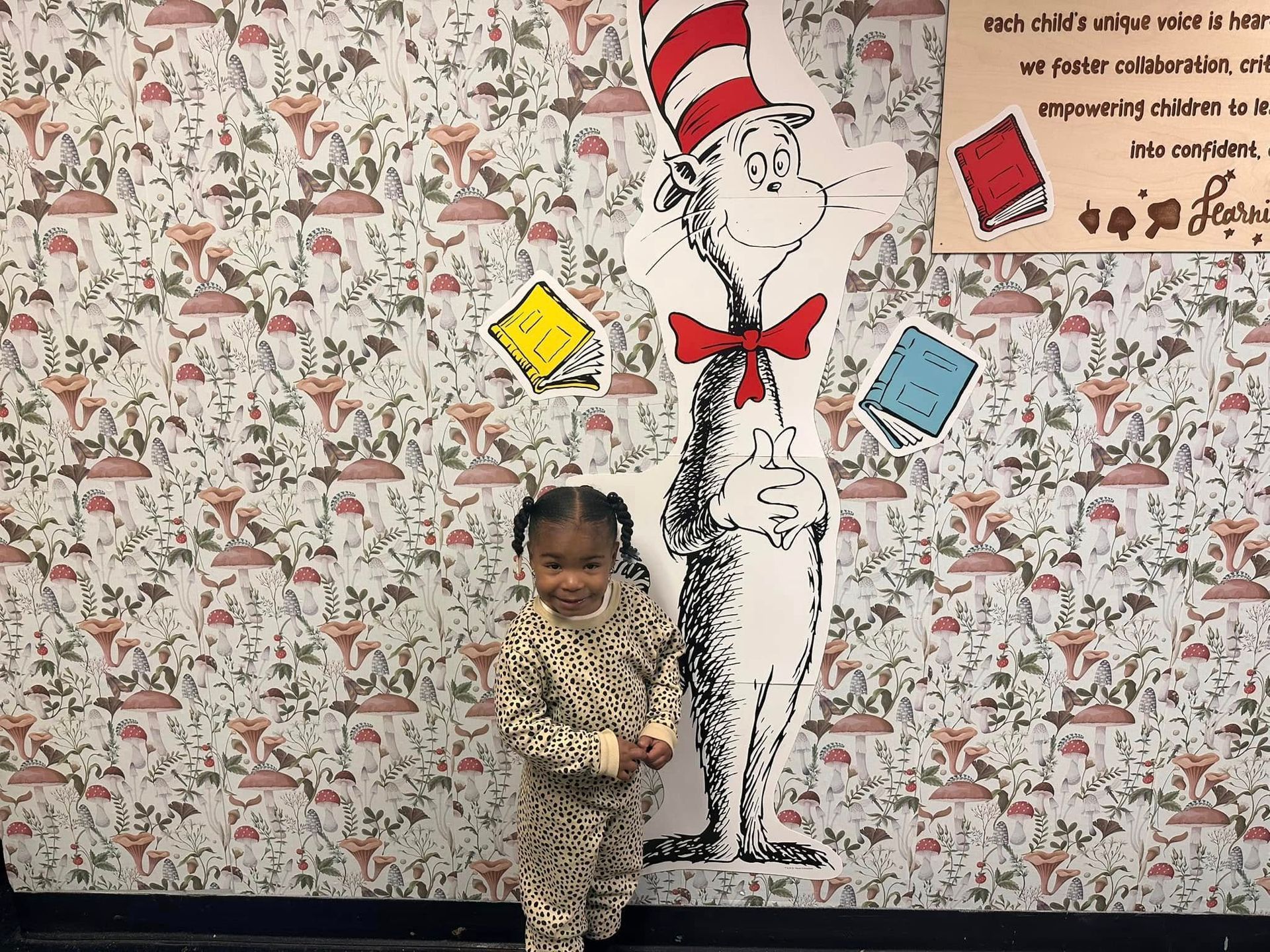 A little girl is standing in front of a cat in the hat mural.