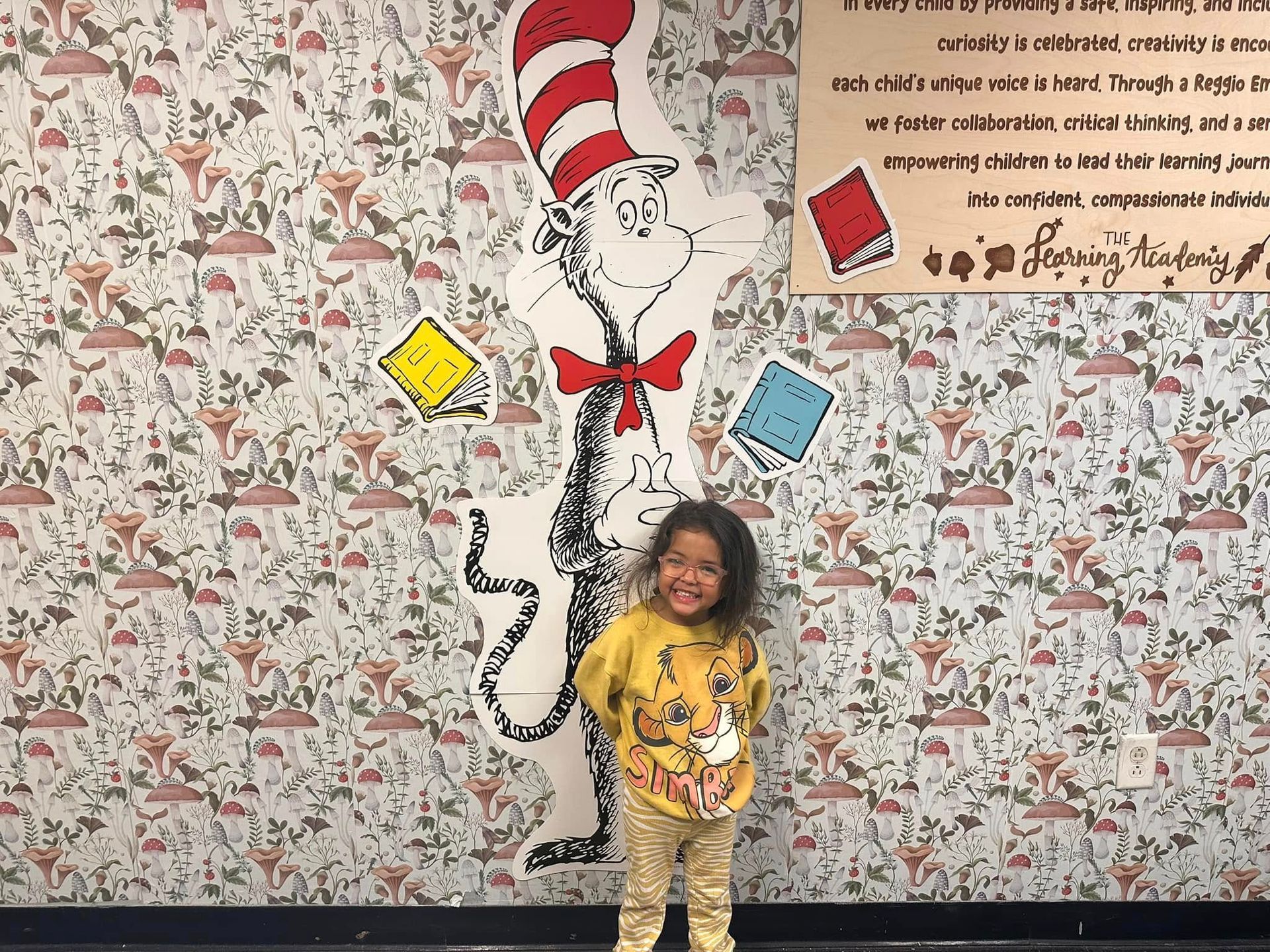 A little girl is standing in front of a cat in the hat mural.