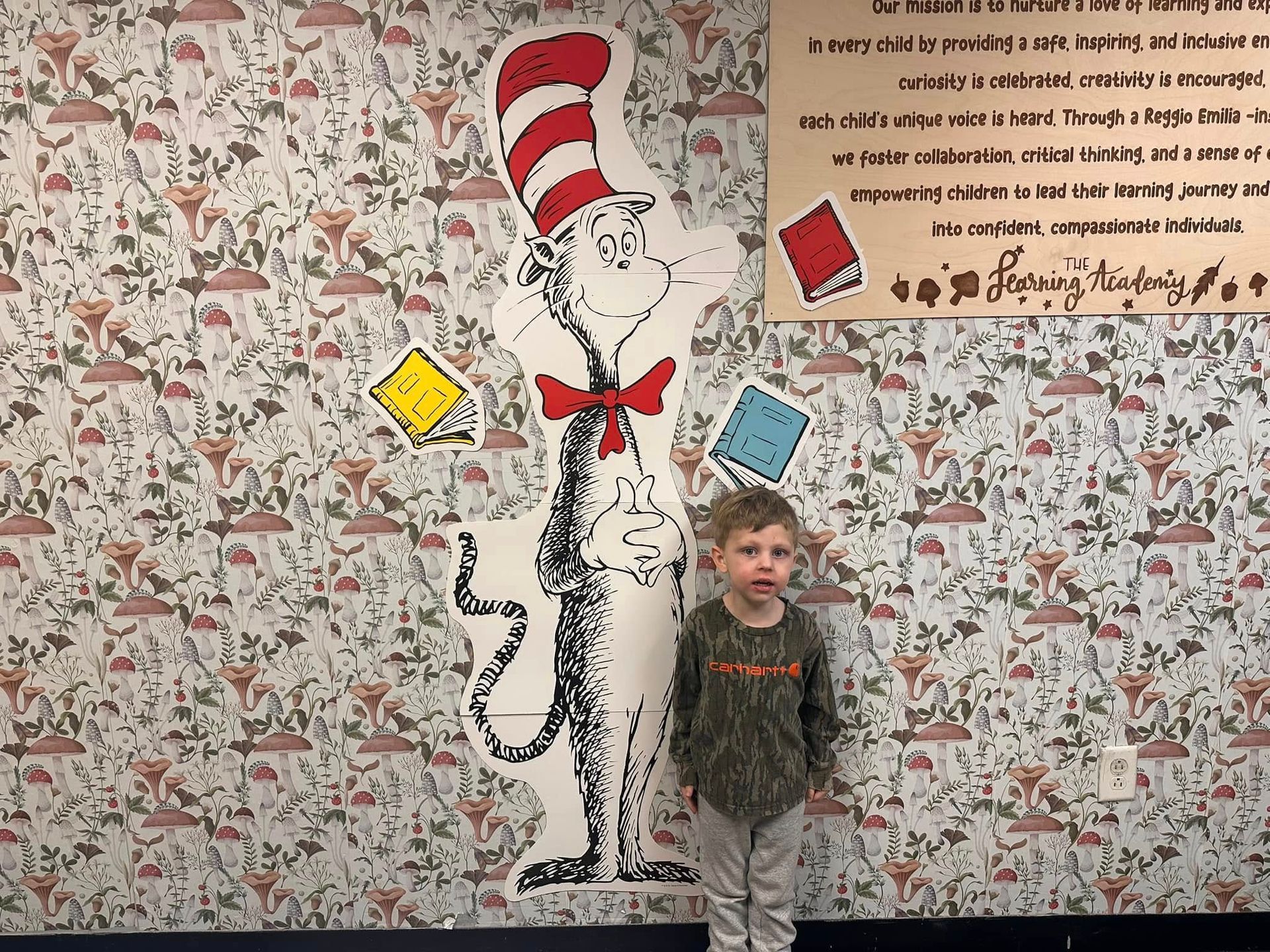 A young boy is standing next to a cat in the hat statue.