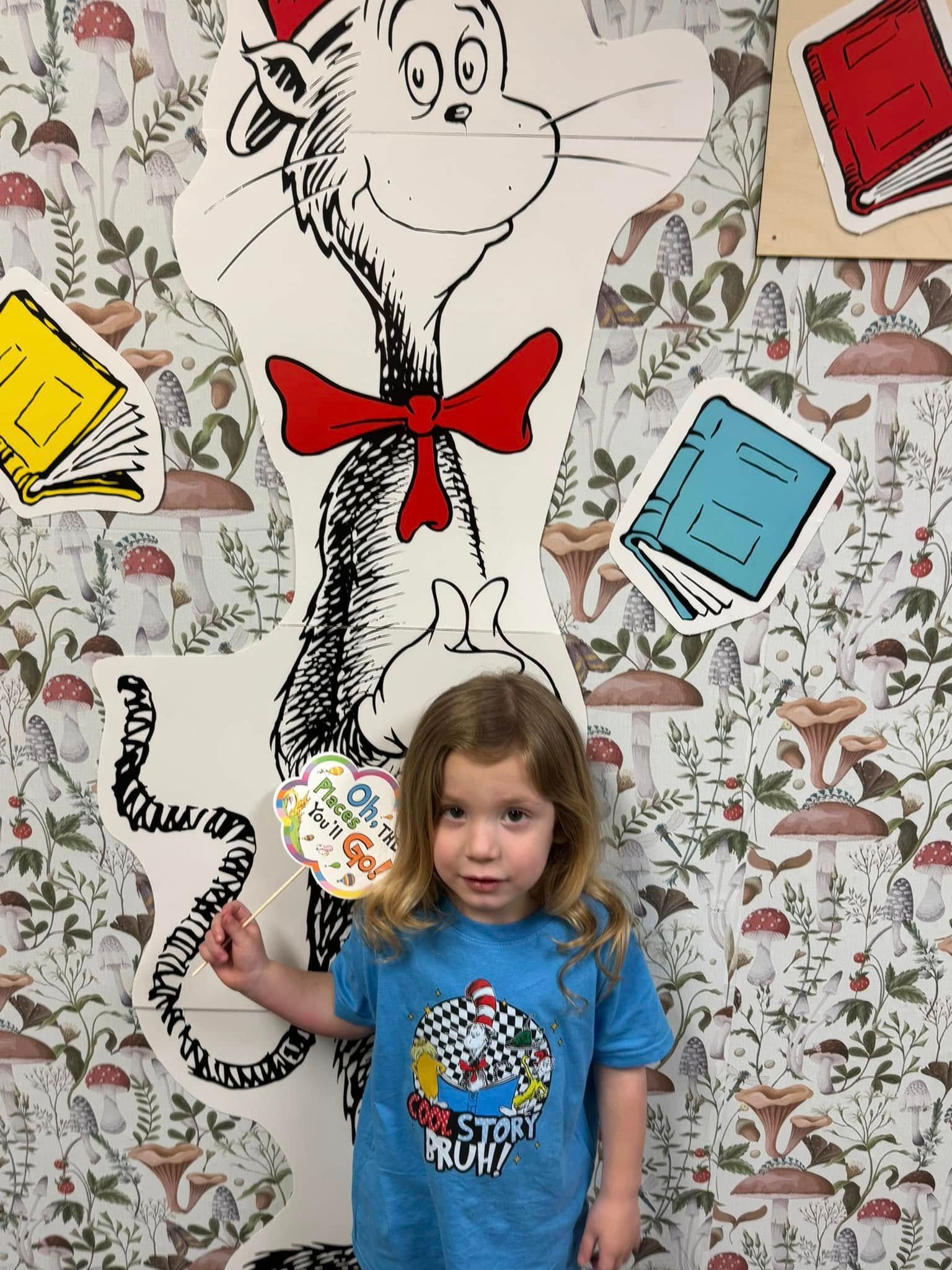 A little girl is holding a lollipop in front of a cat in the hat statue.