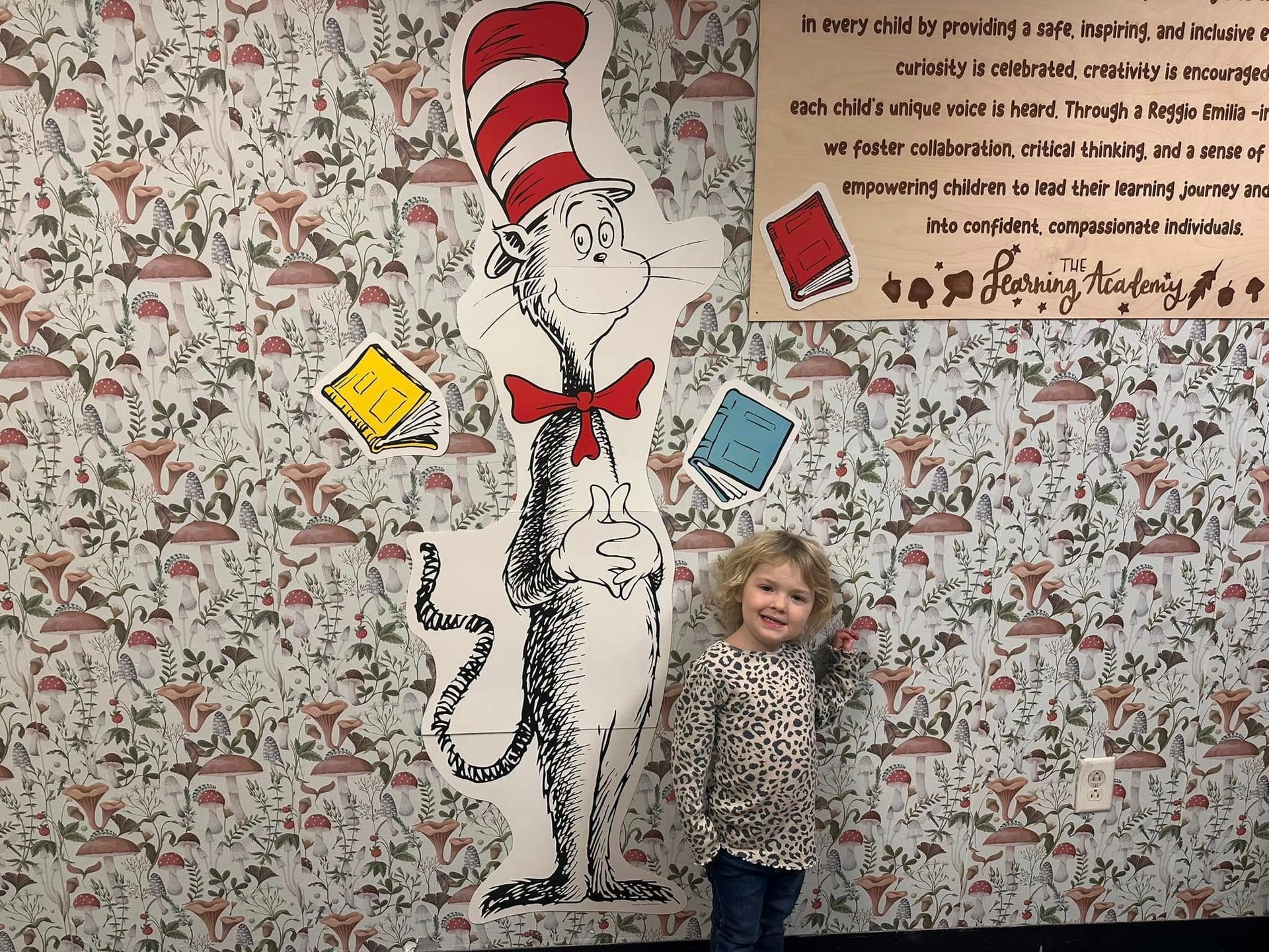 A little girl is standing in front of a cat in the hat mural.