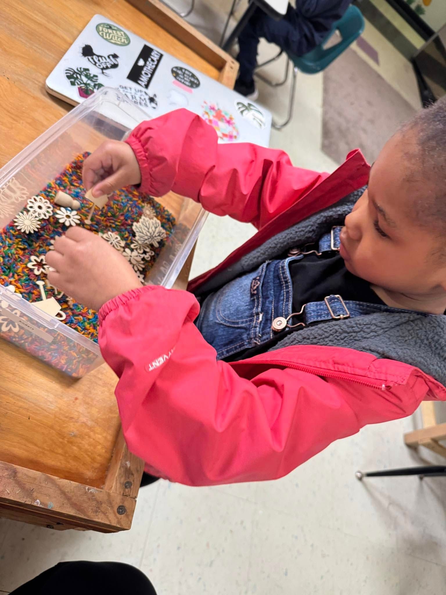 A little girl is sitting at a table playing with sprinkles.
