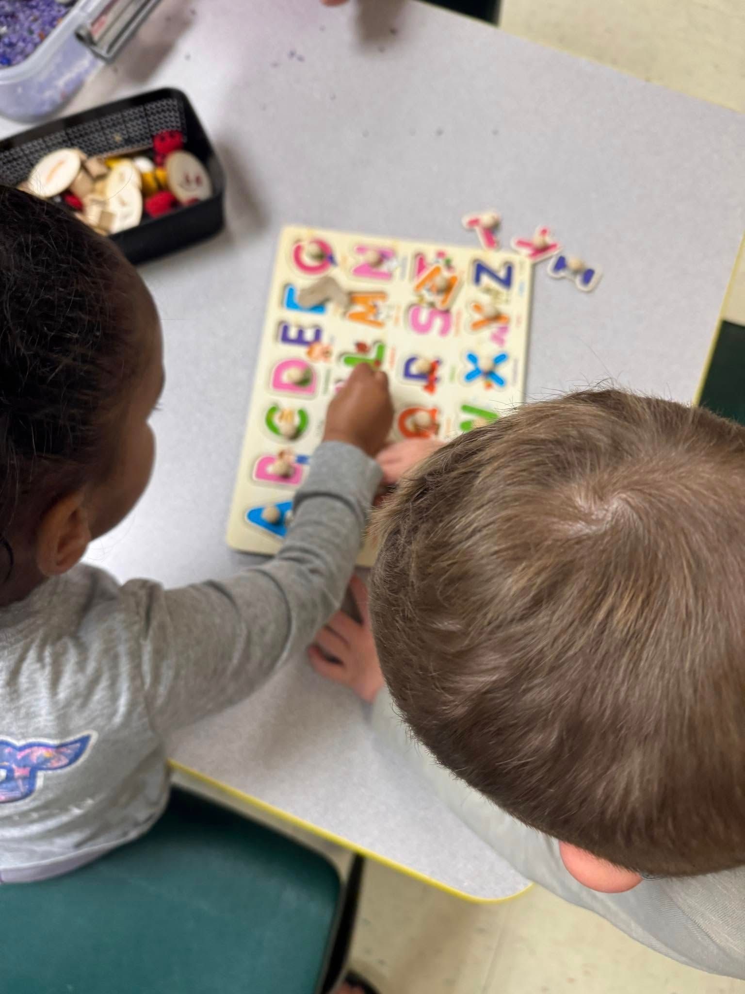 A boy and a girl are playing with an alphabet puzzle.