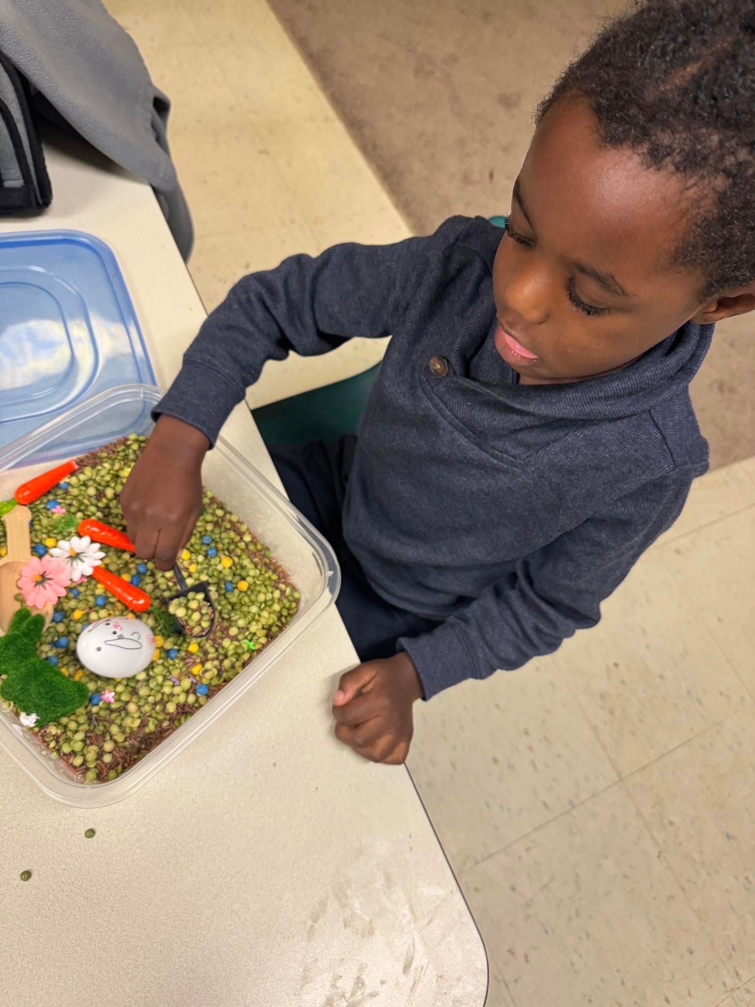 A young boy is playing with a sensory bin filled with rice and sprinkles.