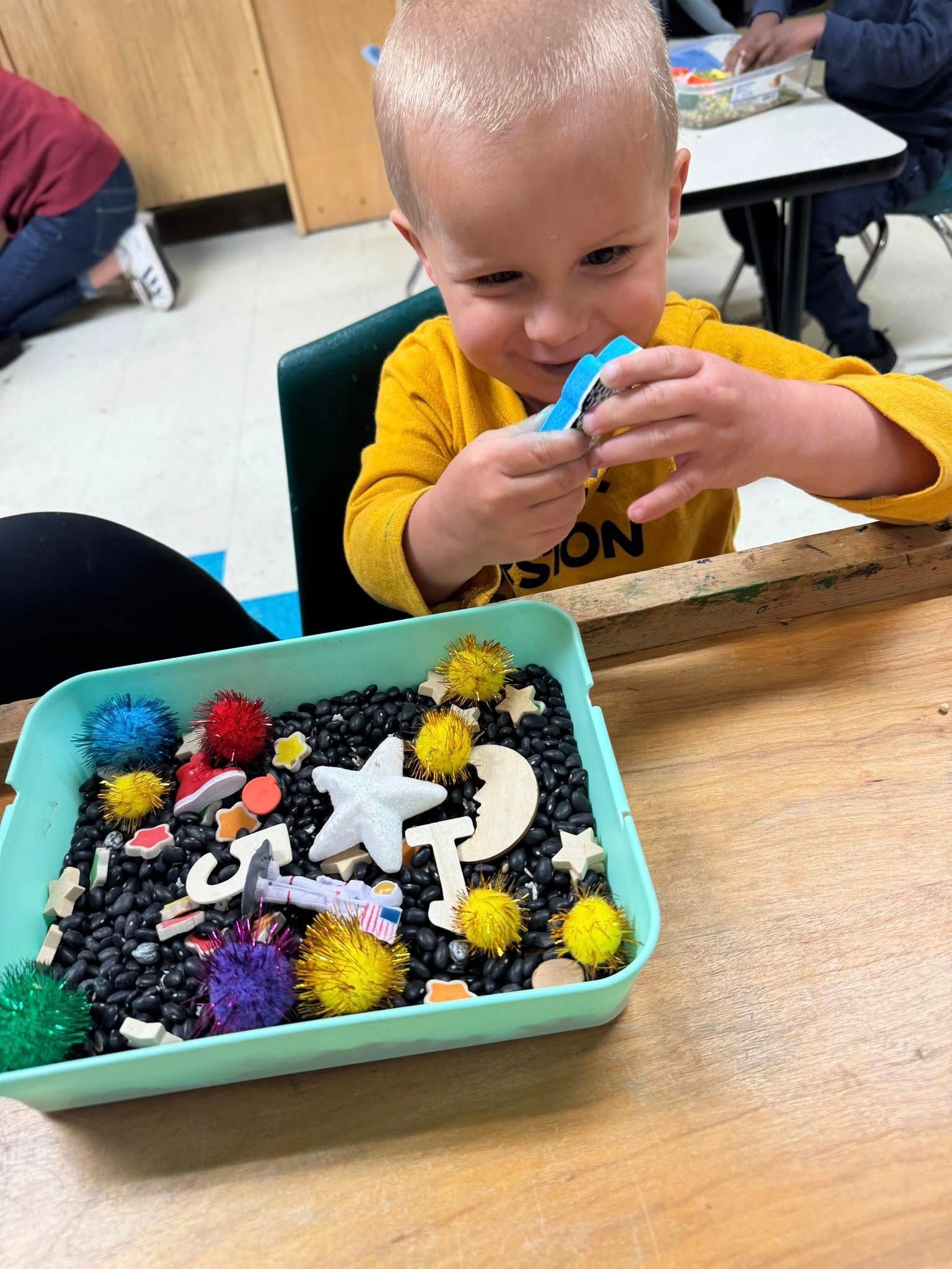 A young boy is sitting at a table playing with a tray of toys.