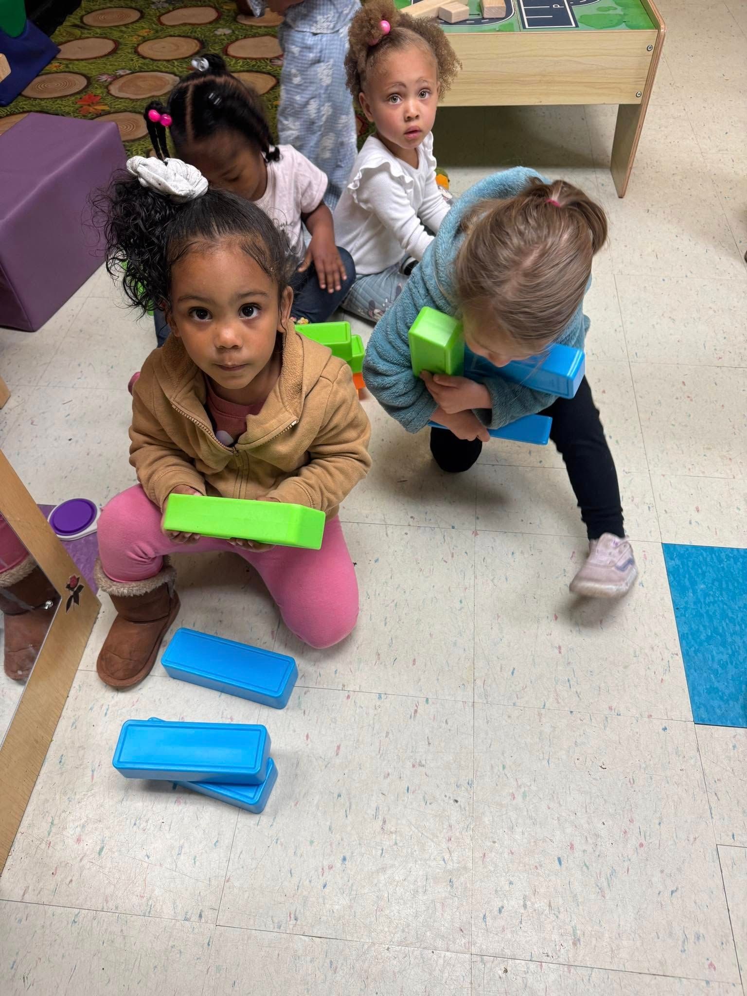 A group of young girls are playing with blocks on the floor.