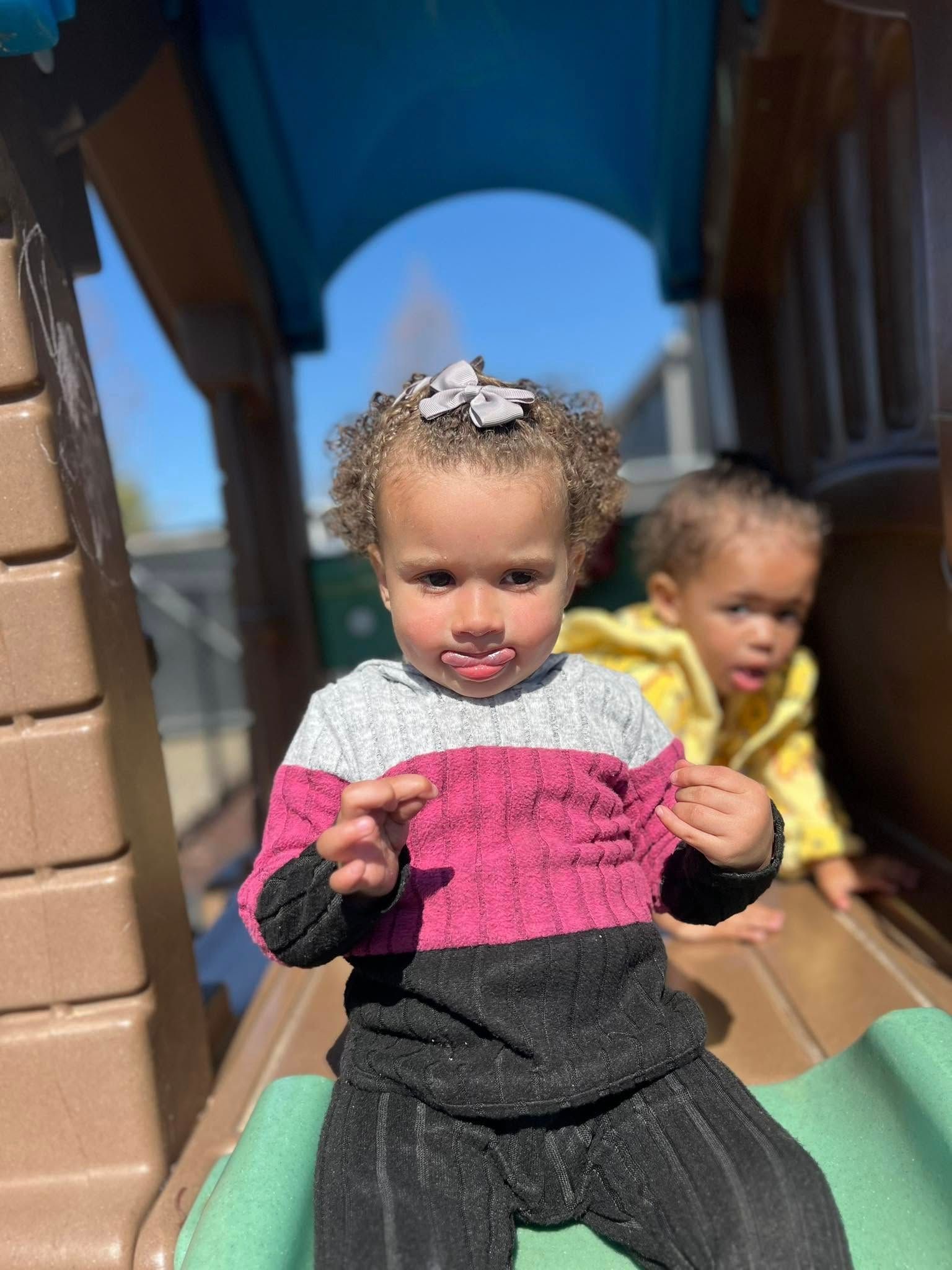 A little girl is sitting on a slide at a playground.