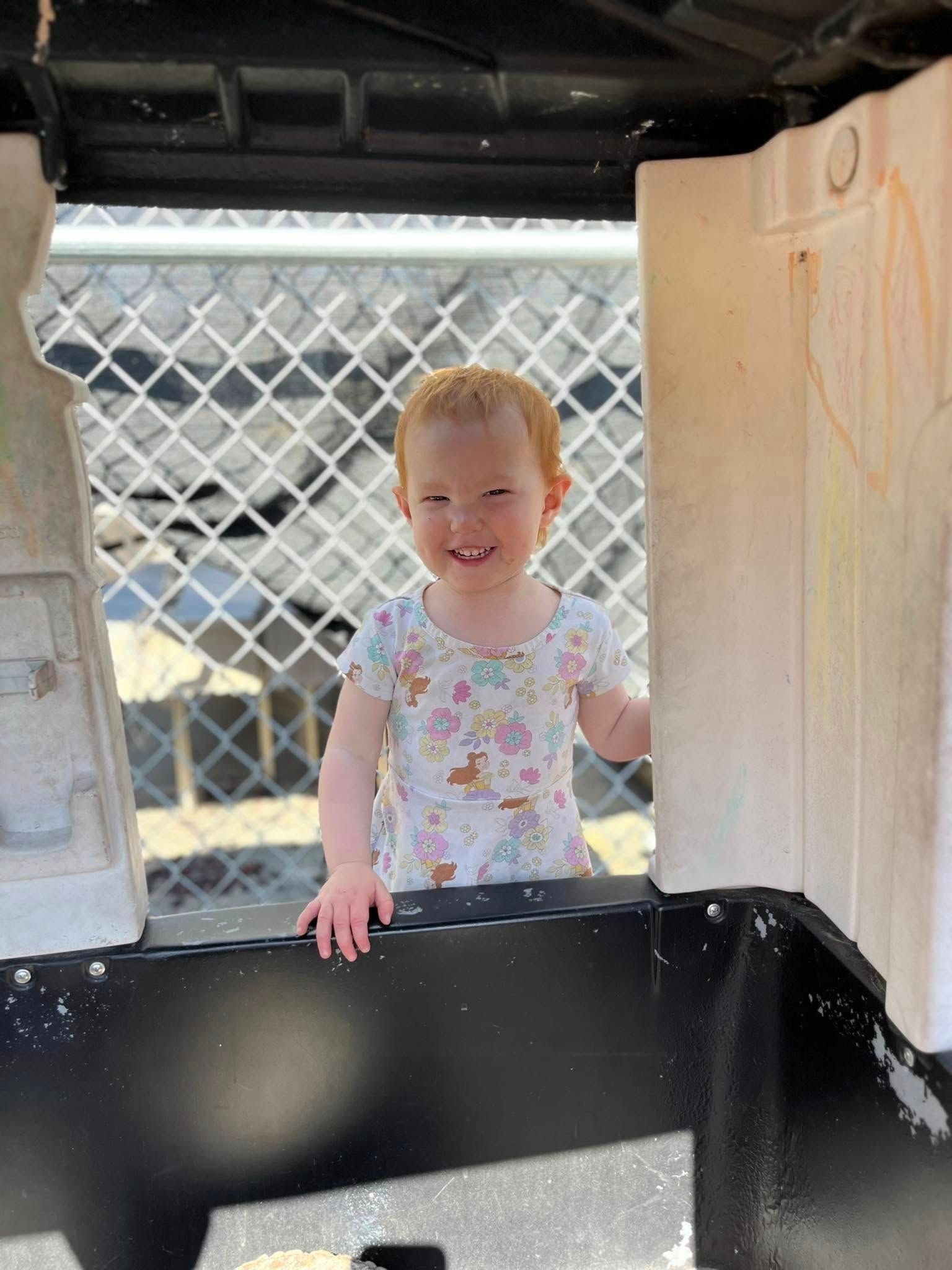 A little girl is standing in a playhouse and smiling.
