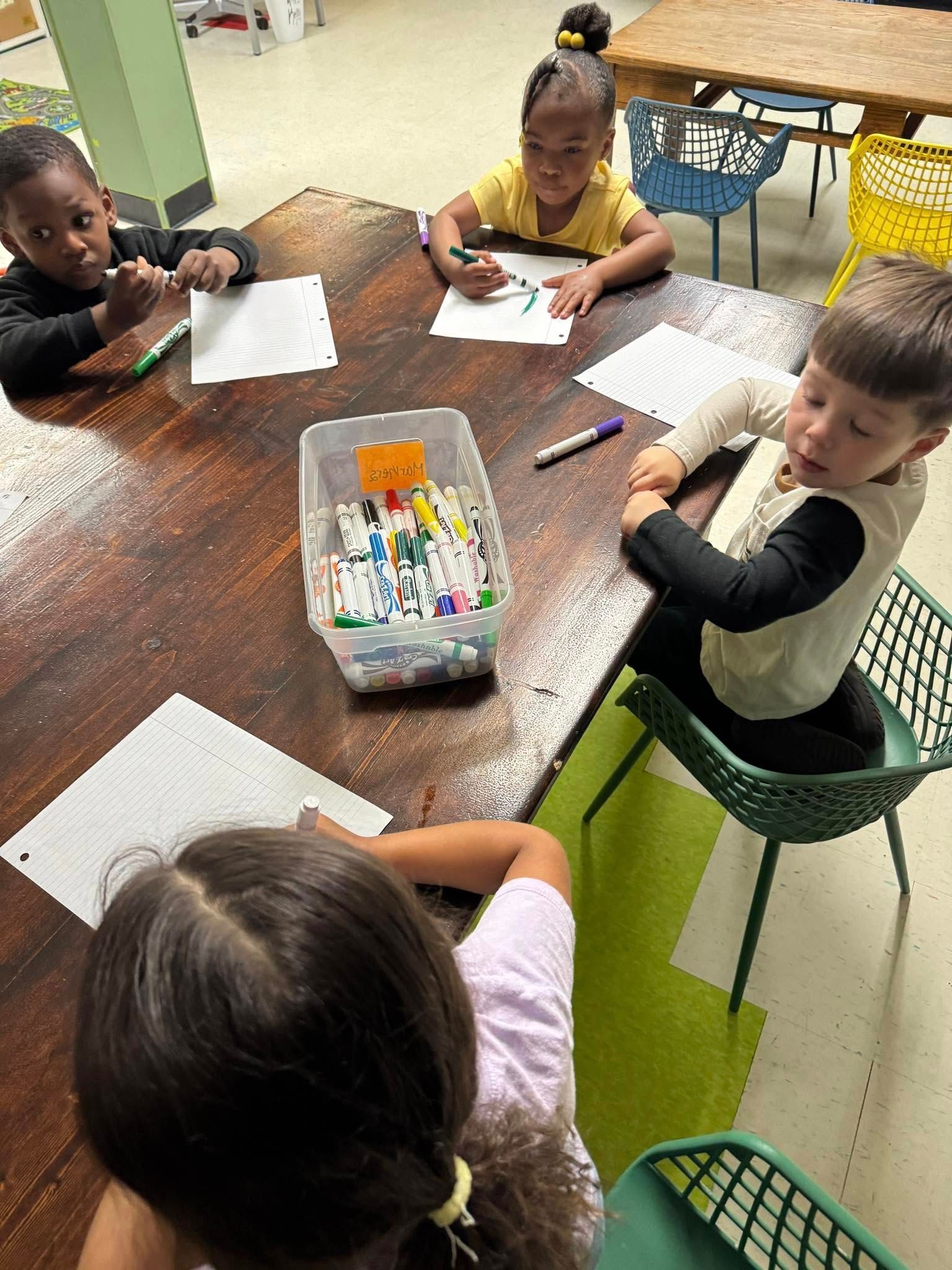 A group of children are sitting around a table drawing with markers.