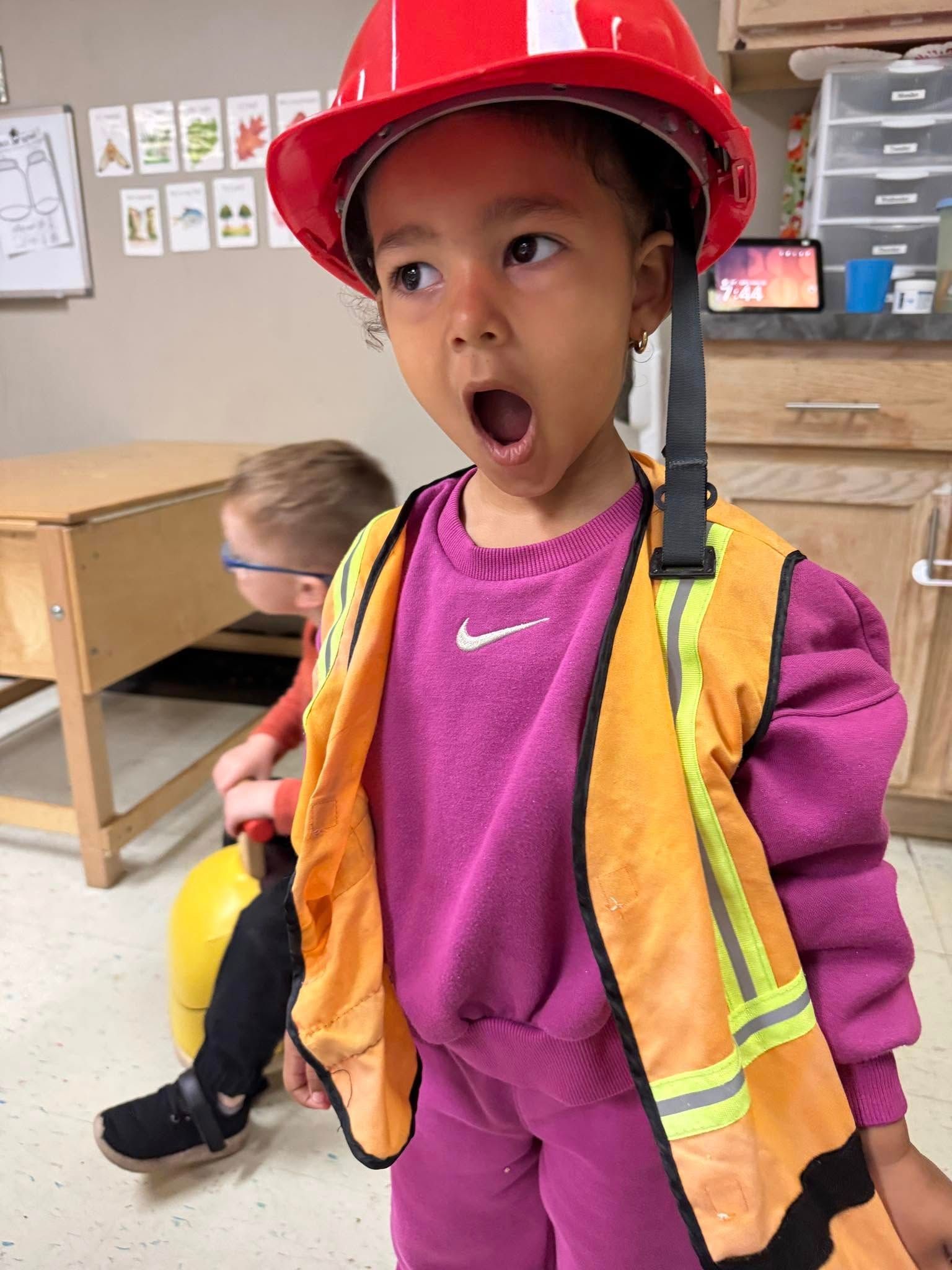 A little girl is wearing a hard hat and safety vest.