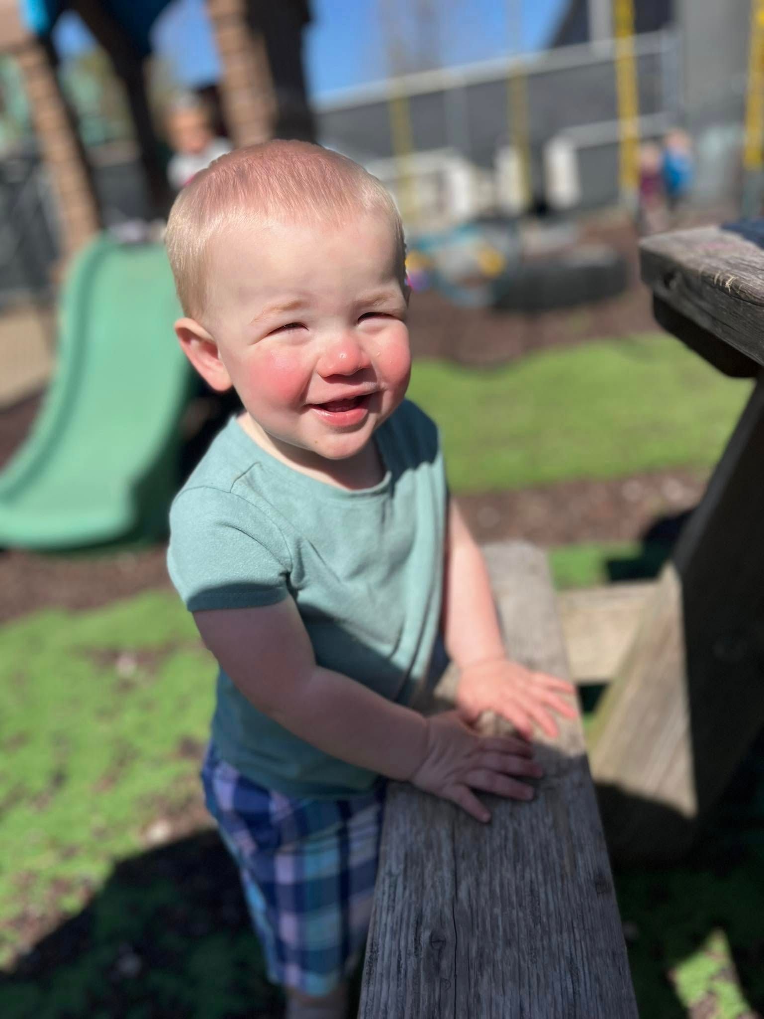 A little boy is standing on a wooden post in a playground.