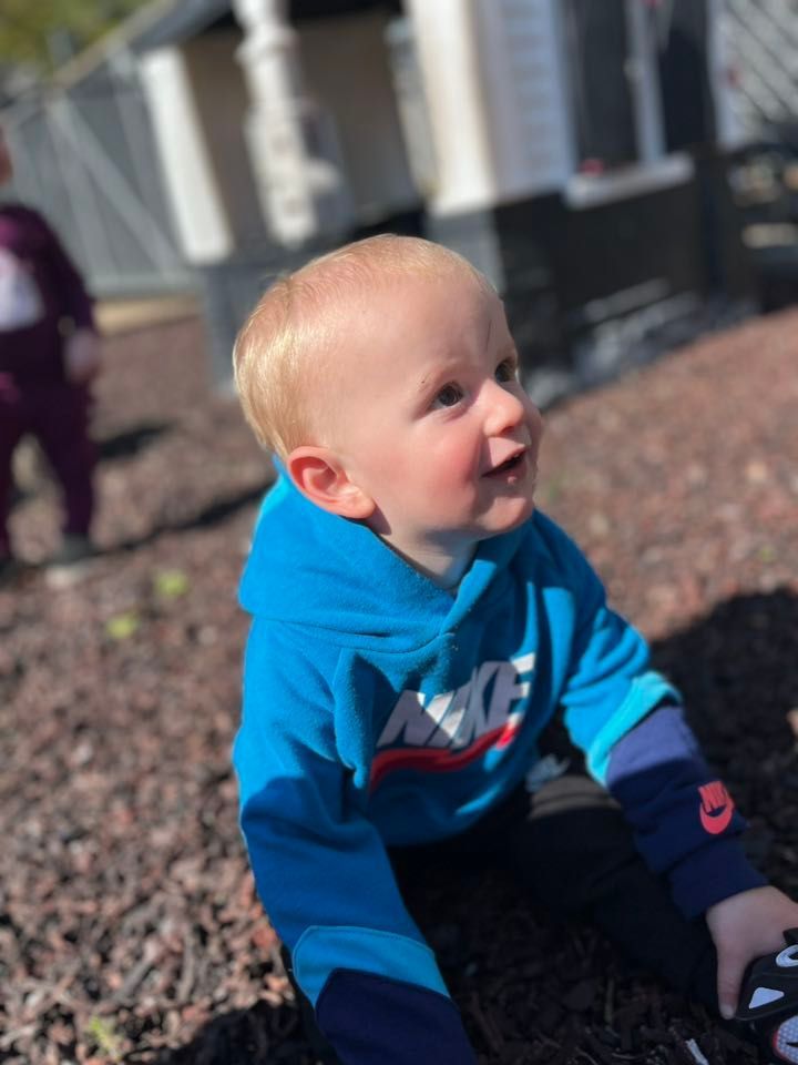 A baby wearing a blue nike hoodie is crawling in the dirt