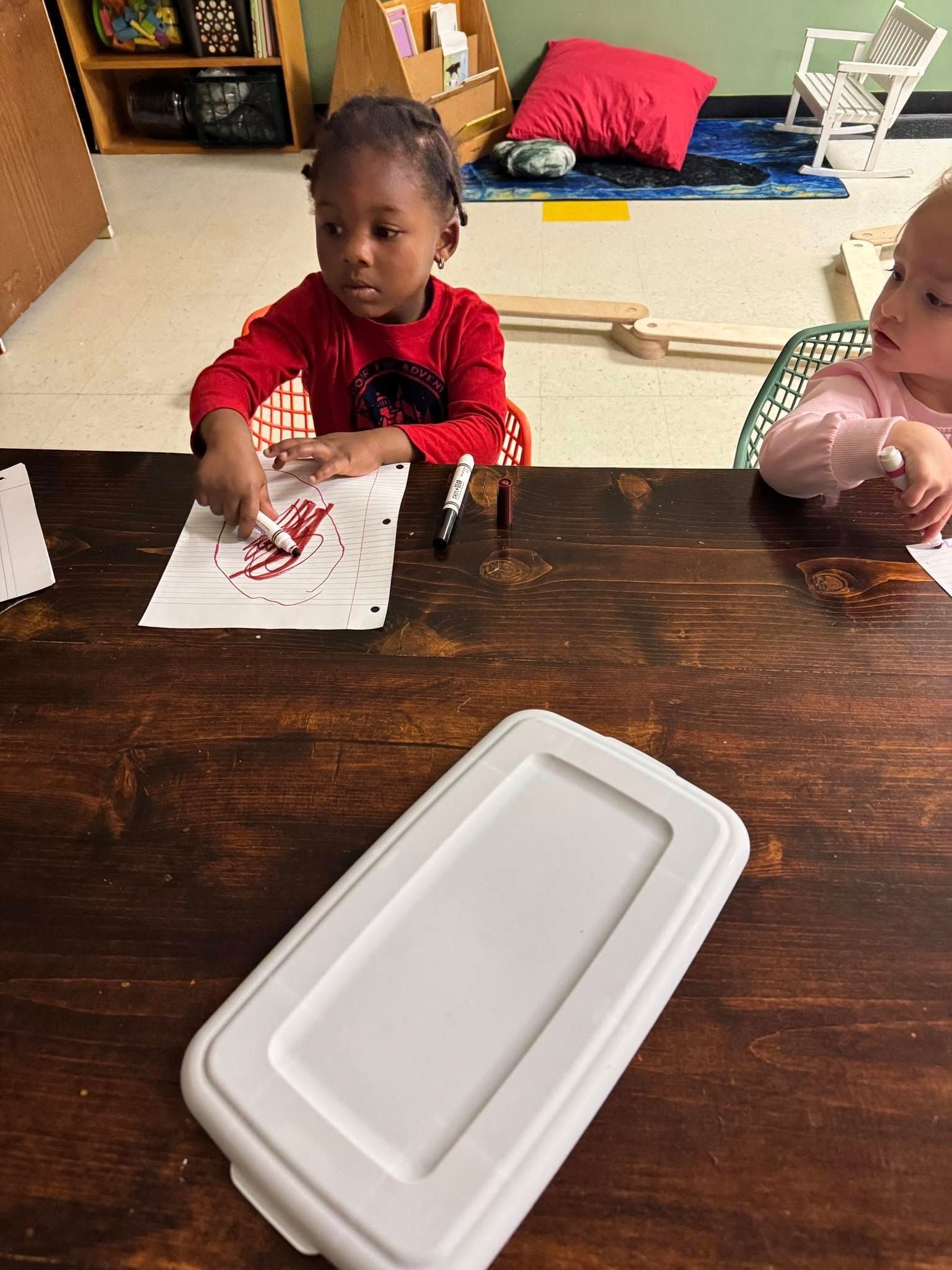 A little girl is sitting at a table with a white lid.