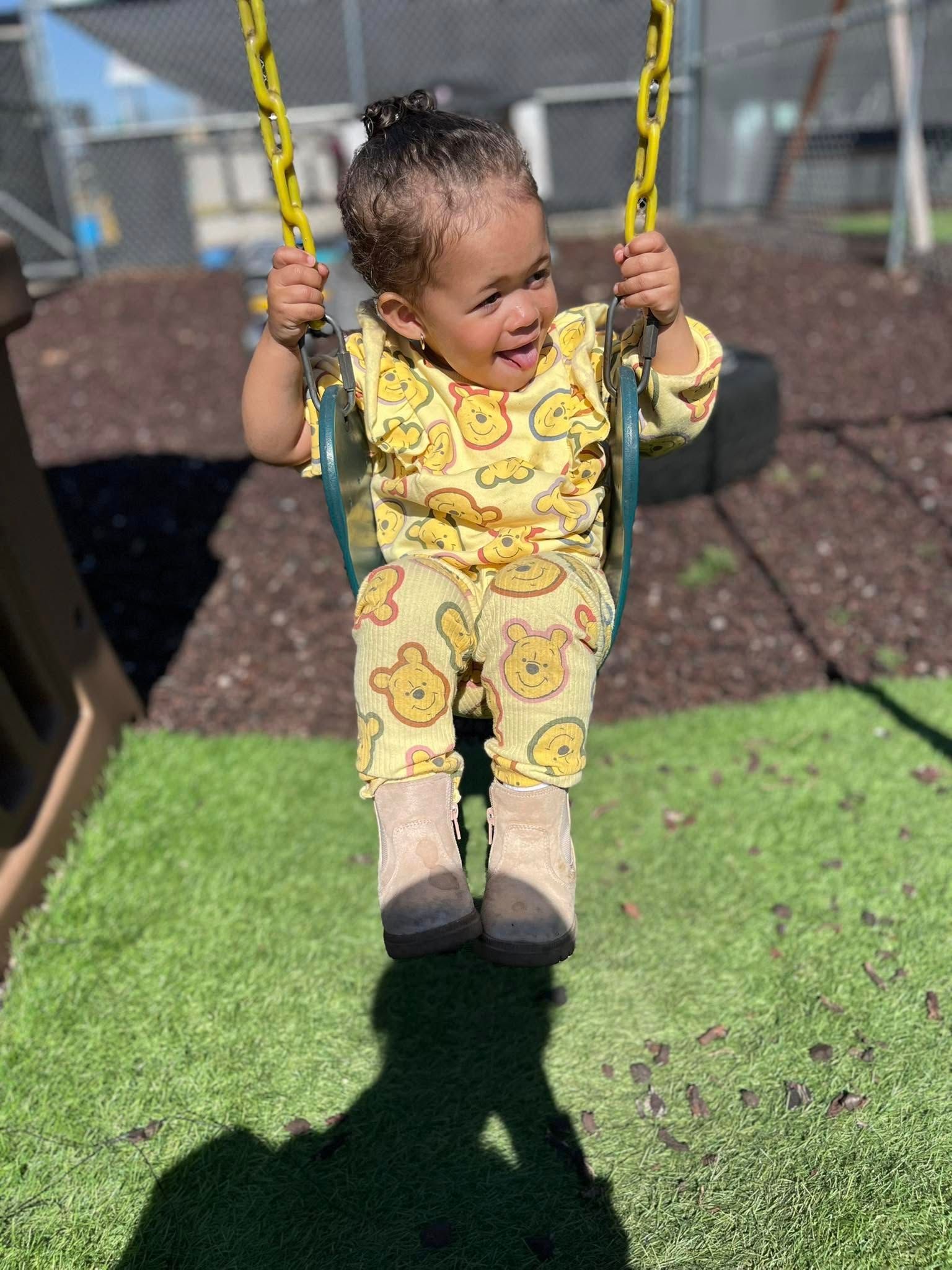 A little girl is sitting on a swing in a park.