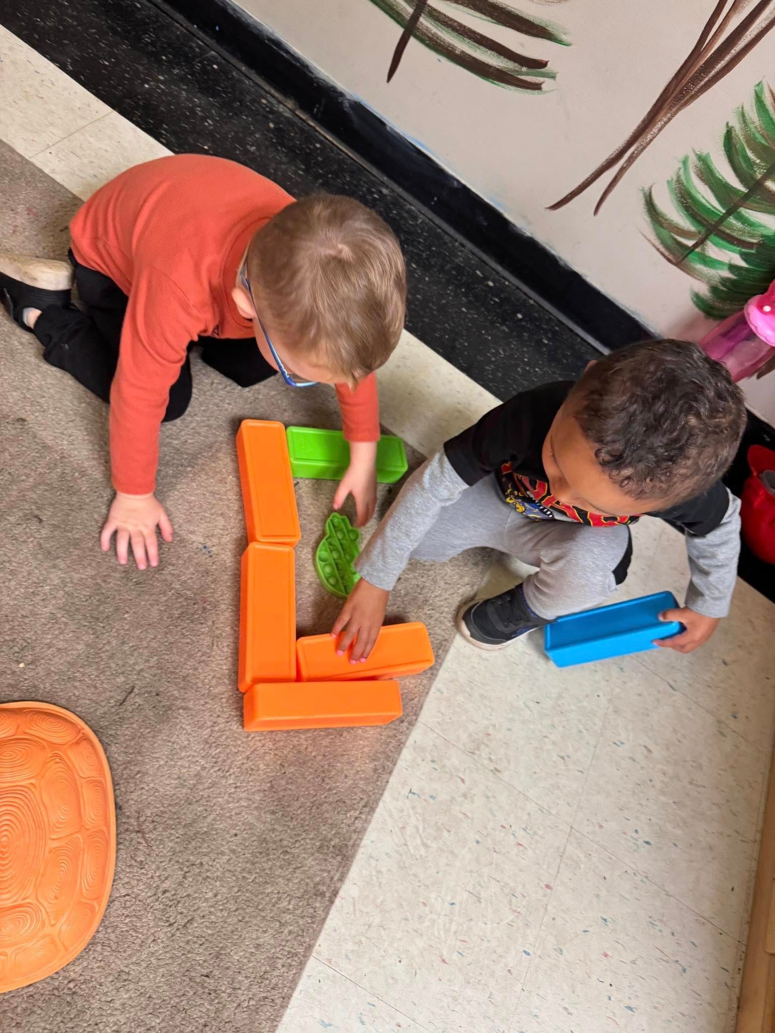 Two young boys are playing with blocks on the floor.