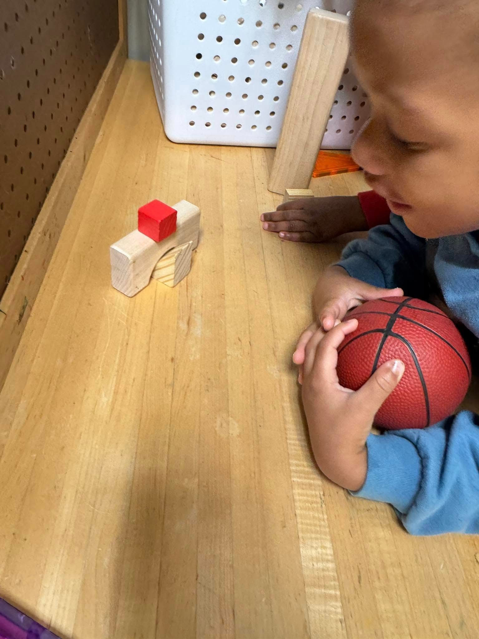 A young boy is playing with a basketball on a wooden table.
