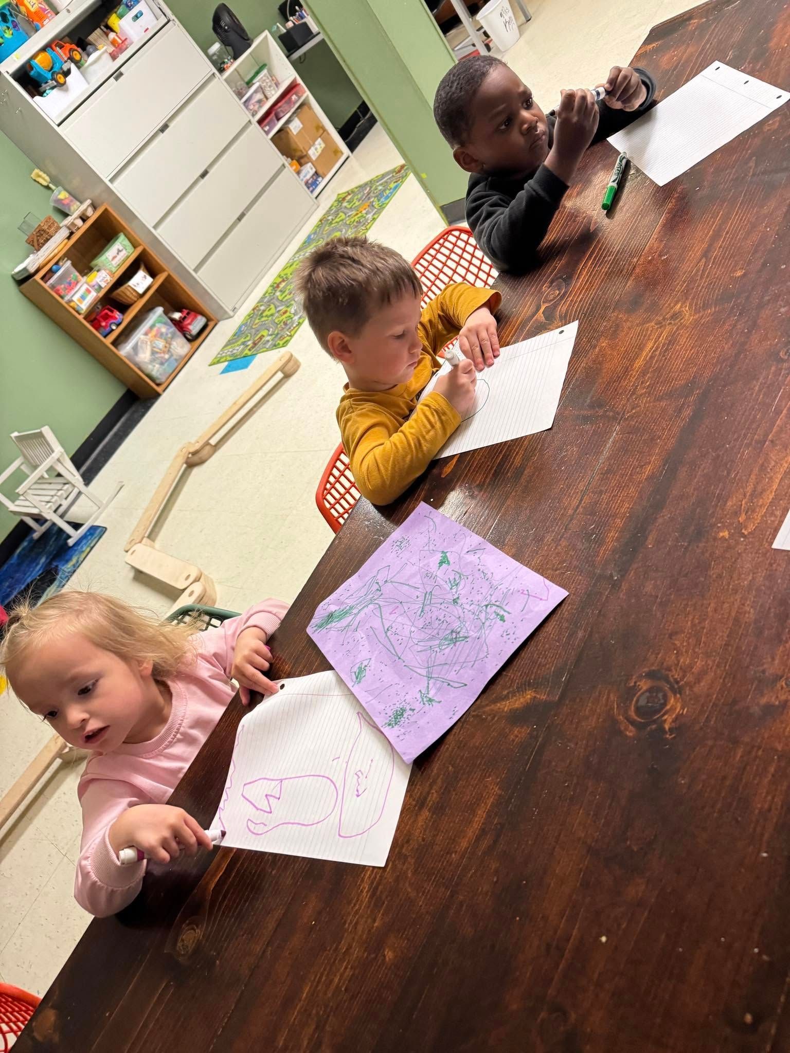 Three children are sitting at a table with papers on it.