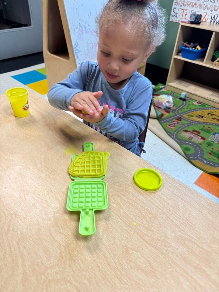 A little girl is sitting at a table playing with play dough.