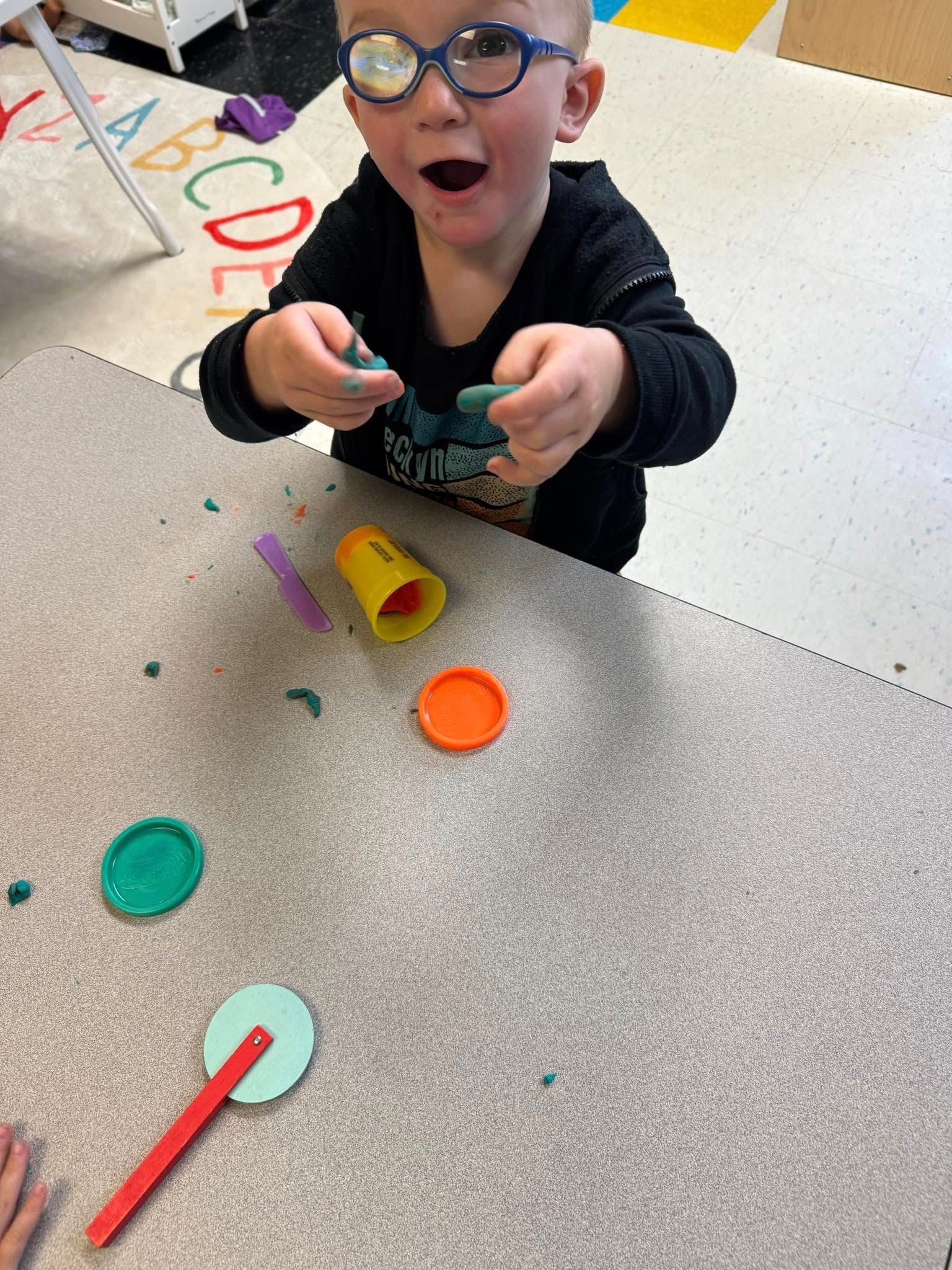 A young boy wearing glasses is playing with play dough at a table.
