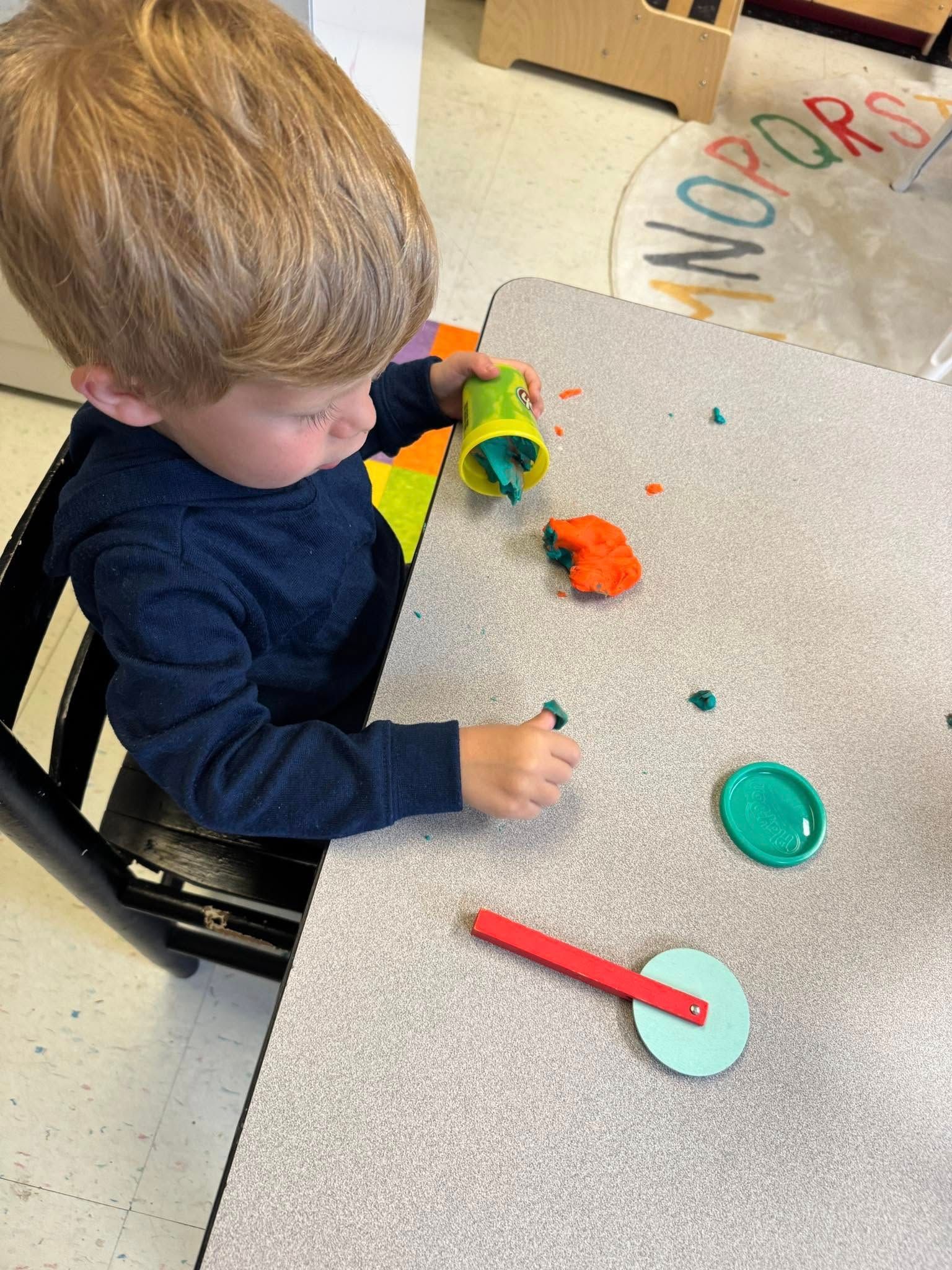 A young boy is sitting at a table playing with play dough.