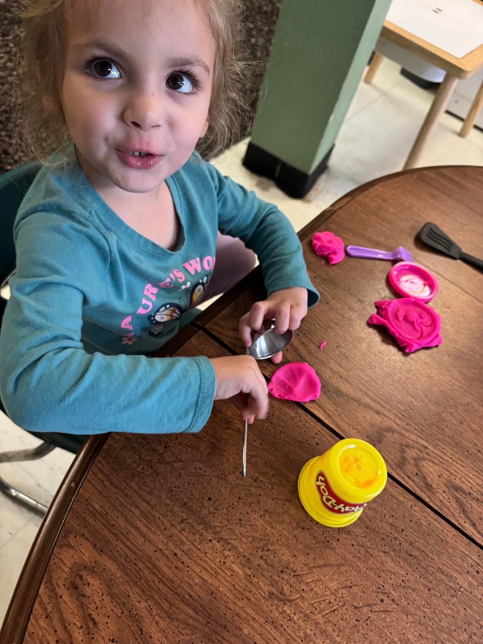 A little girl is sitting at a table playing with play dough.